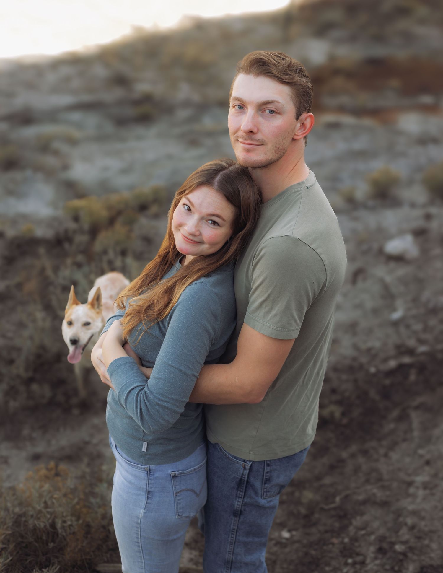 Romantic couple portraits with their dog on rocky ground during golden hour.