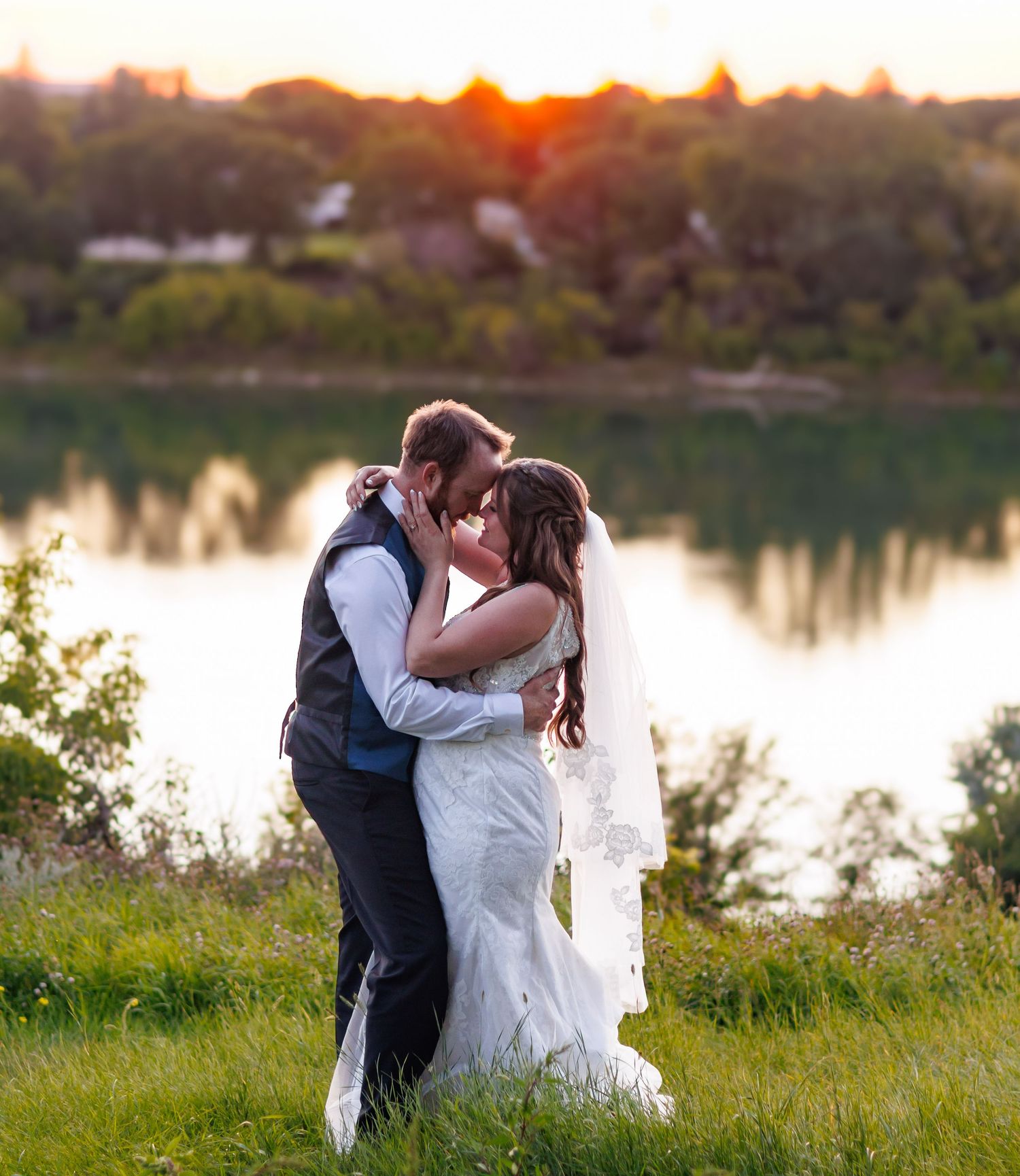 Sunset wedding portraits by a lake with warm orange glow.