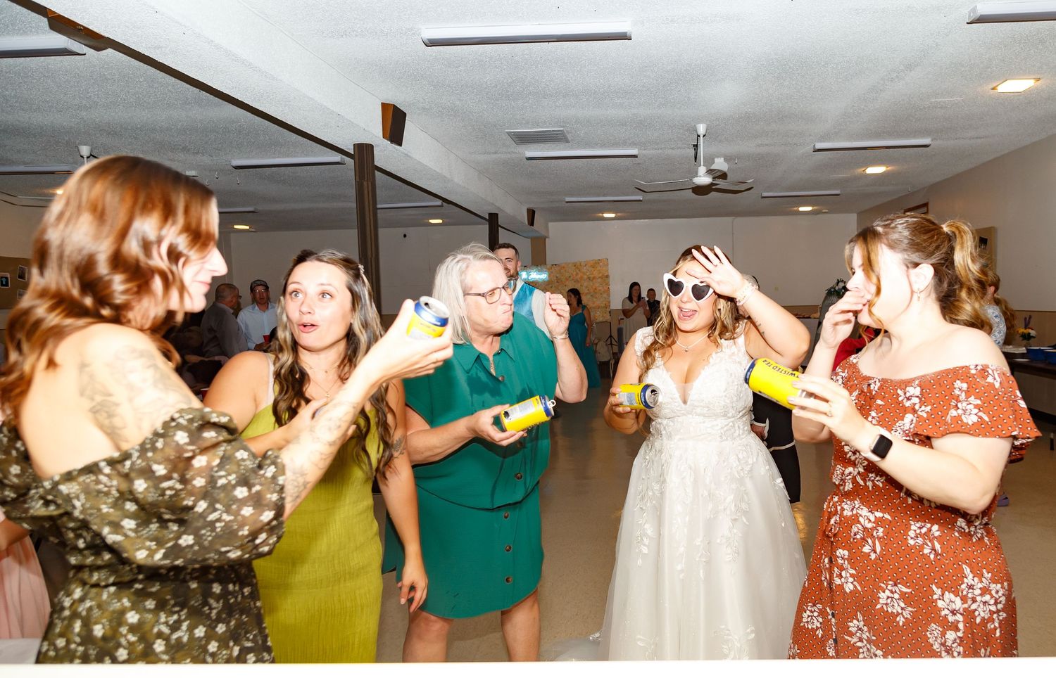 Wedding party dancing and celebrating in a reception hall with fluorescent lighting.
