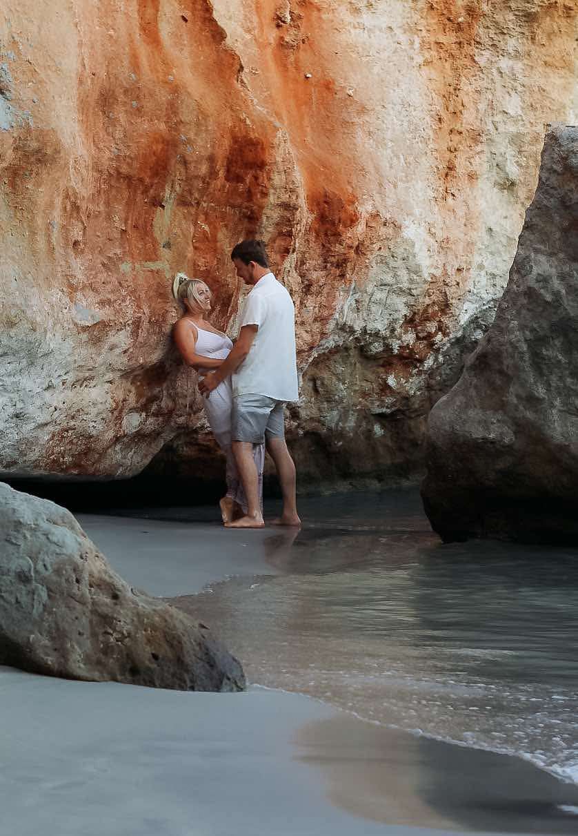 A romantic beach photo against dramatic orange limestone cliffs and turquoise waters.