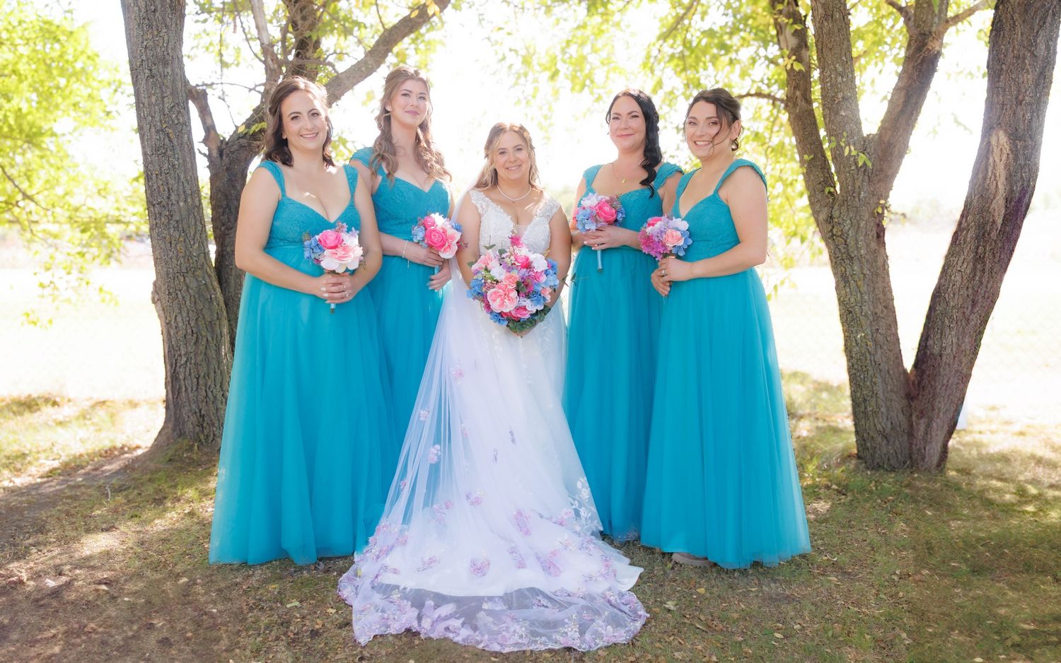 Wedding party group photo under trees with bridesmaids in matching turquoise dresses.