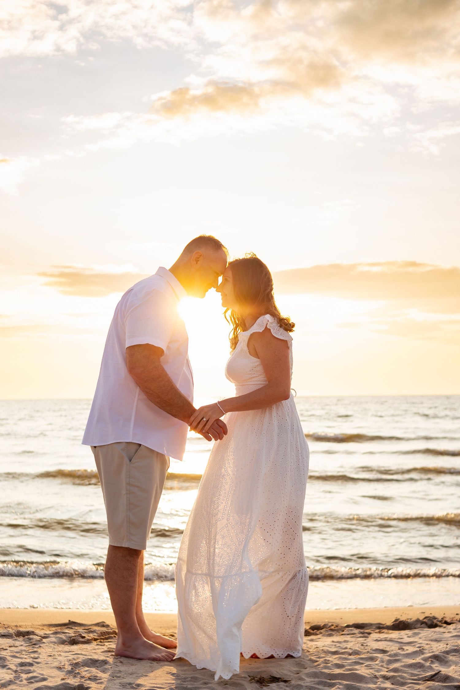 Silhouetted couple sharing intimate moment on beach at sunset.