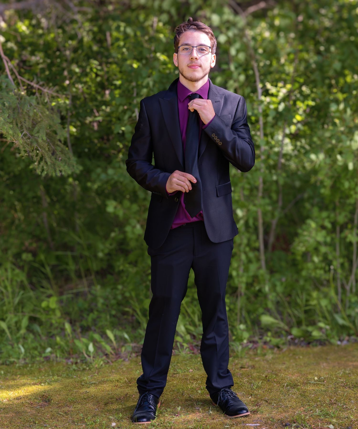 Person in a dark suit striking various poses against a natural outdoor backdrop.