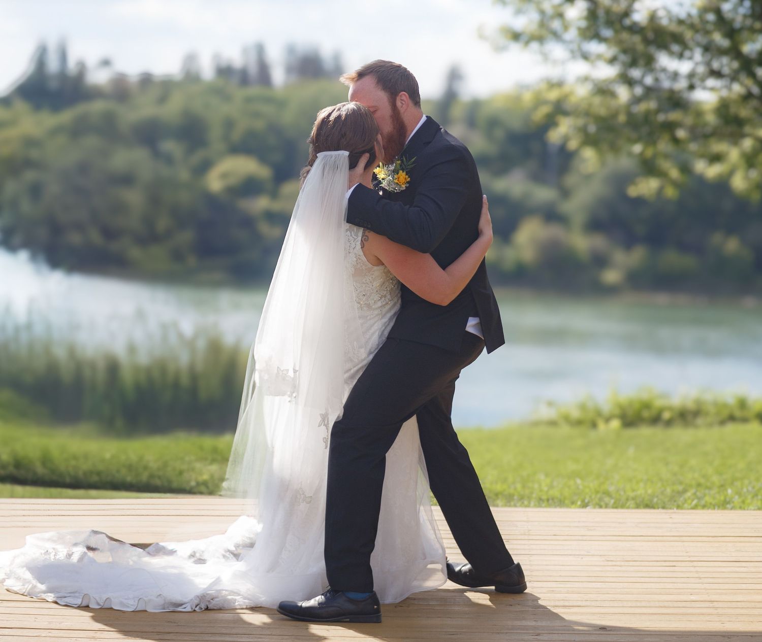 Wedding couple sharing romantic moments on wooden dock by the lake.