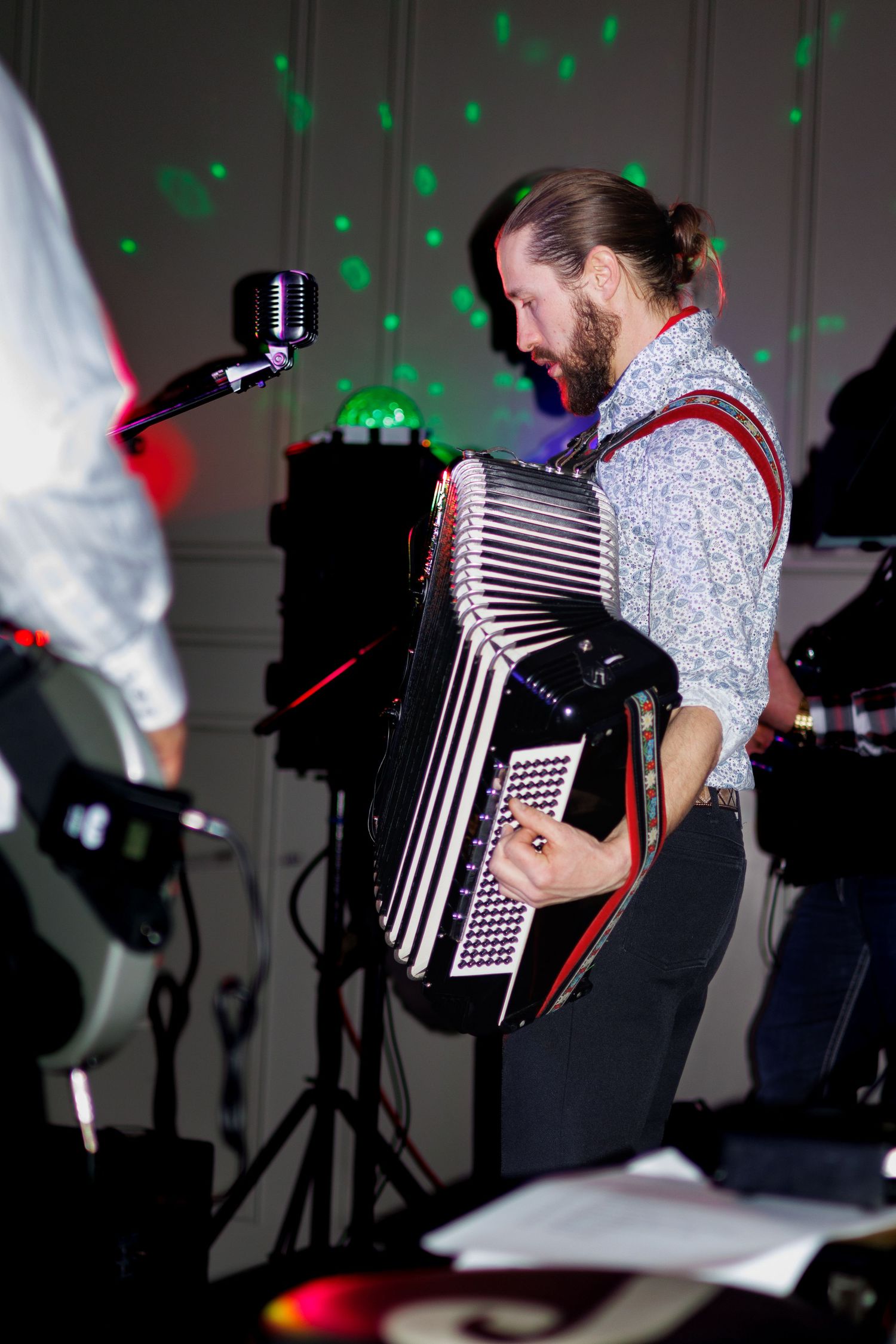 Musician performs with an accordion under green stage lighting at an indoor event.