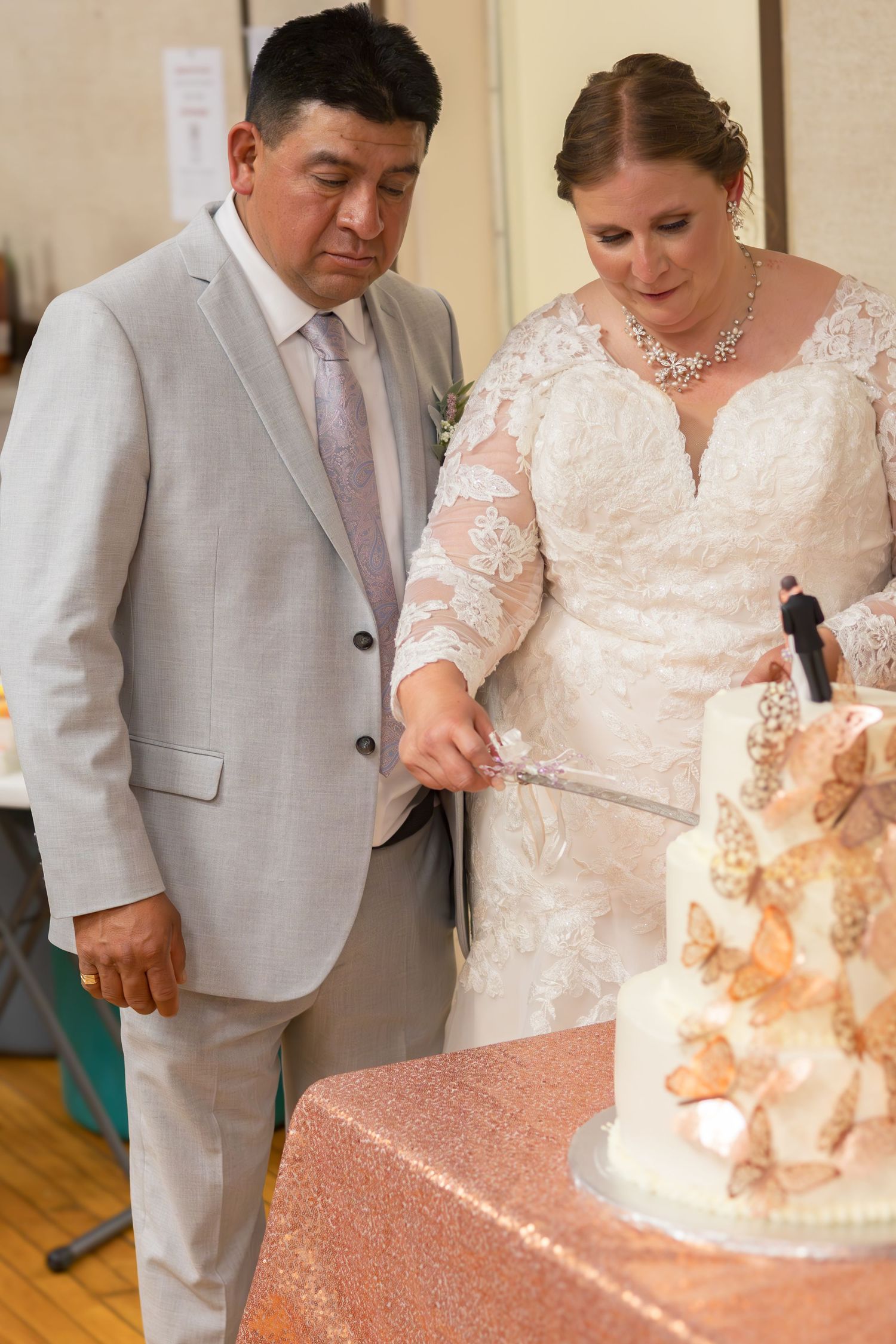A couple prepares to cut their beautiful butterfly-adorned wedding cake together.