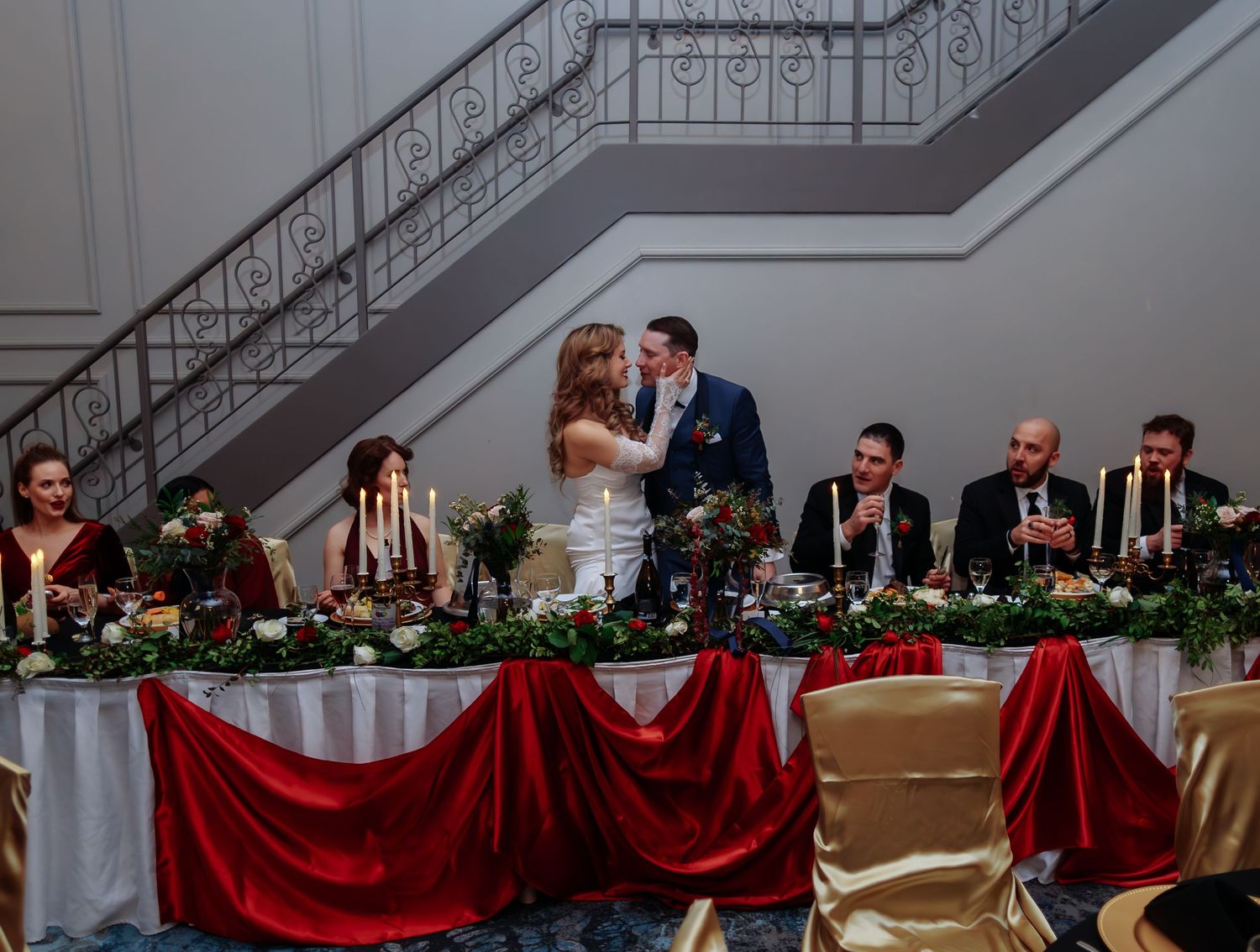 An elegant wedding reception with red and white decor and a head table adorned with greenery garlands.