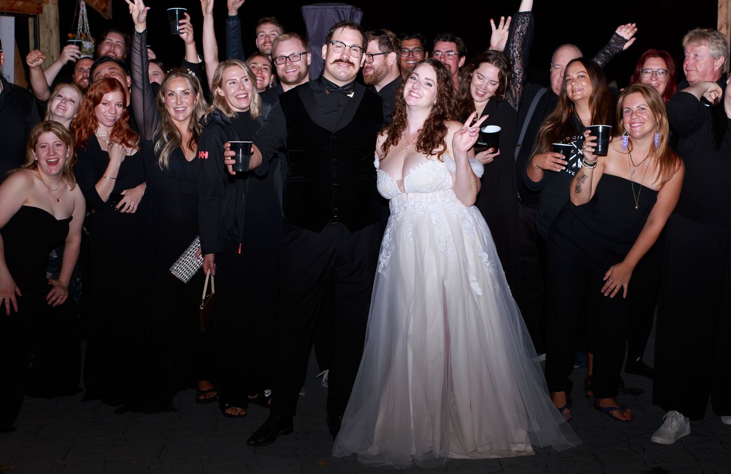 Wedding reception guests dancing and celebrating on a dark dance floor.