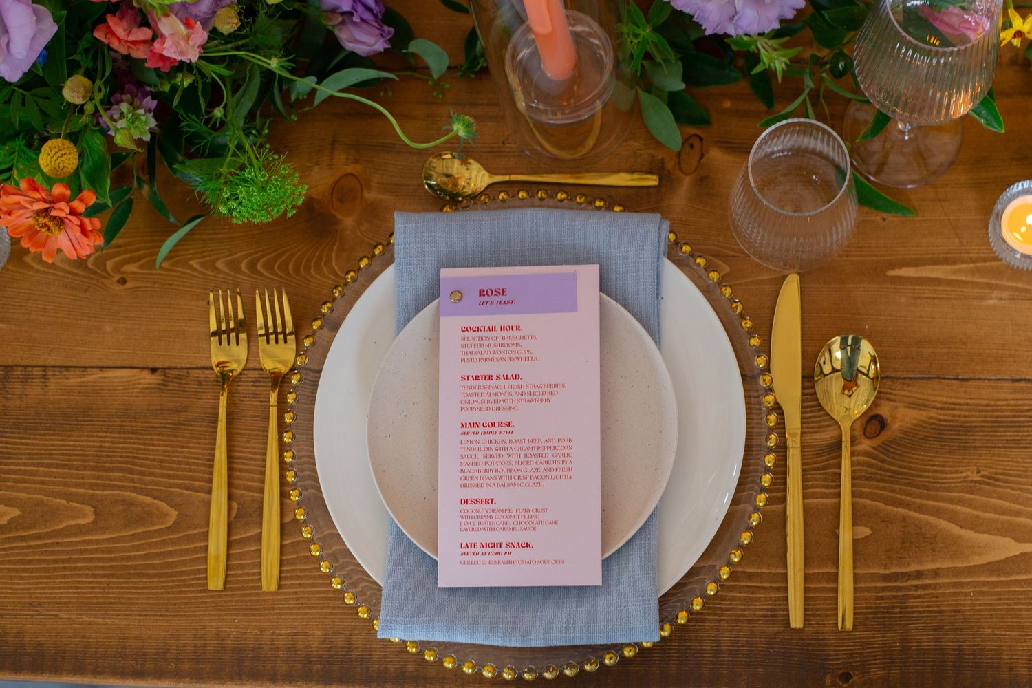 Wedding reception table settings with pink menus and gold cutlery on wooden tables.