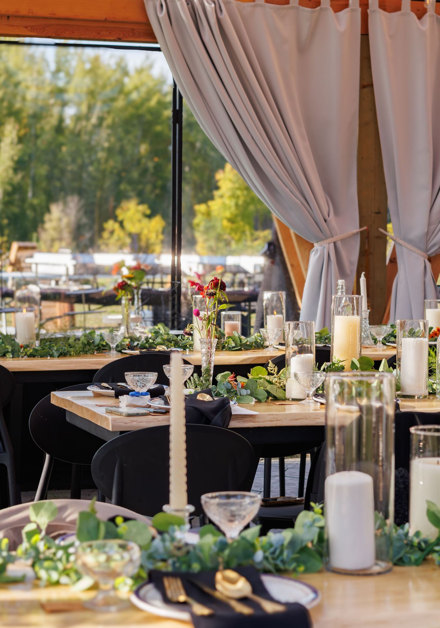 Wedding reception tables set up under white drapes with natural lighting and greenery accents.