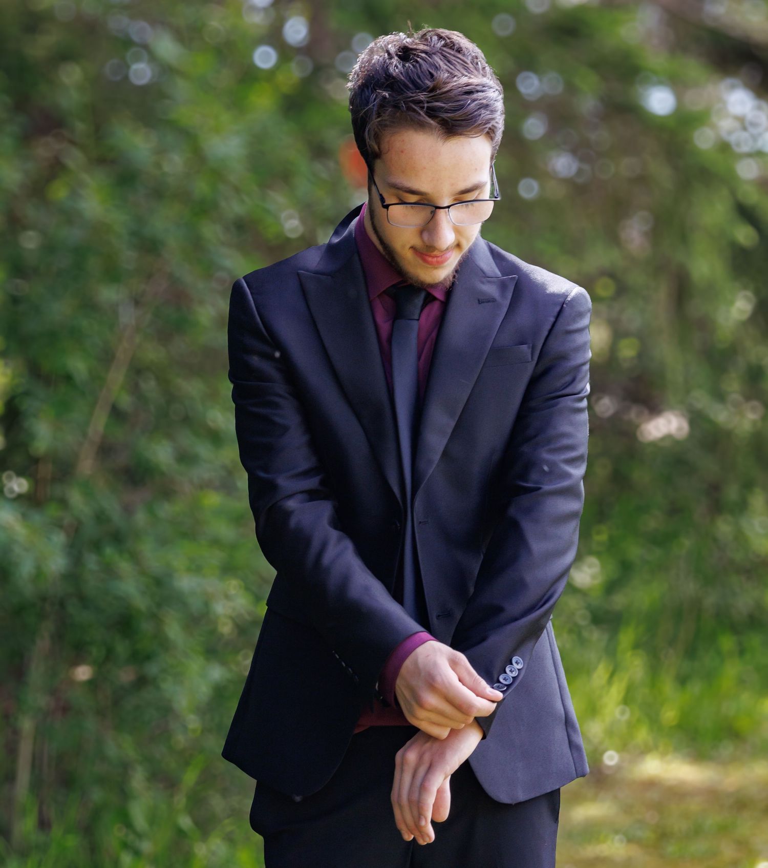 Person in a navy suit adjusting their cuffs while standing in a garden setting.