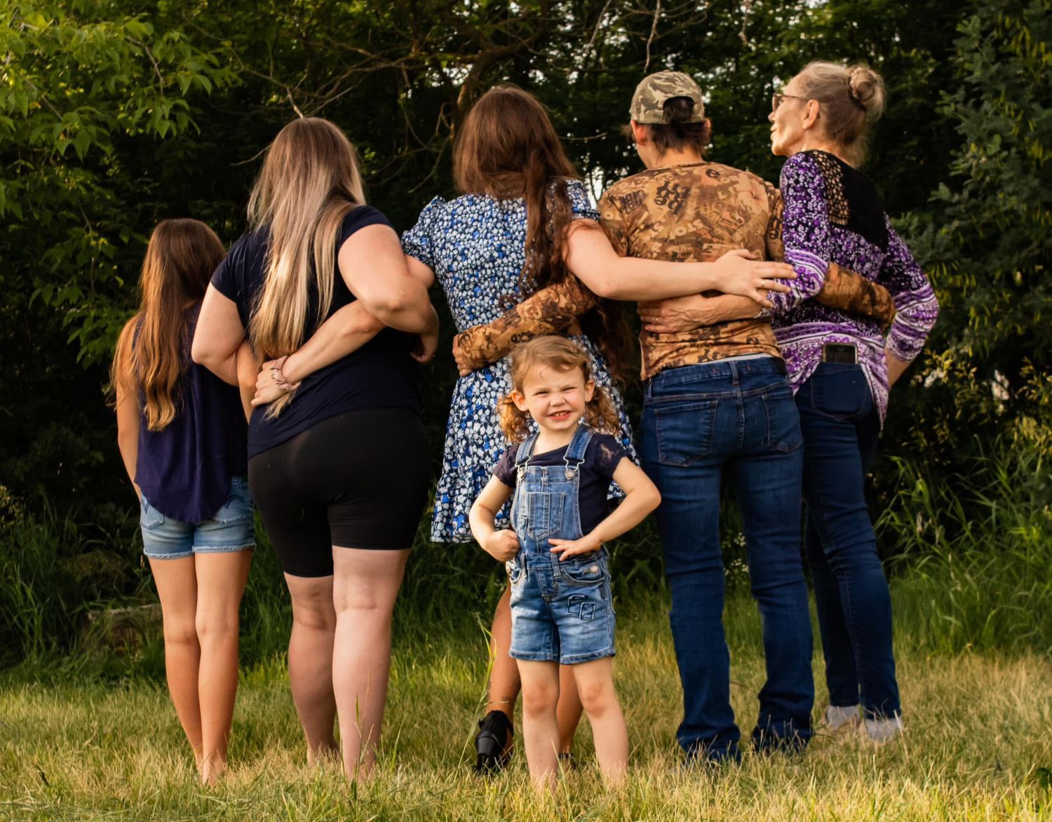 A candid family moment captured from behind as they stand together in a field at sunset.