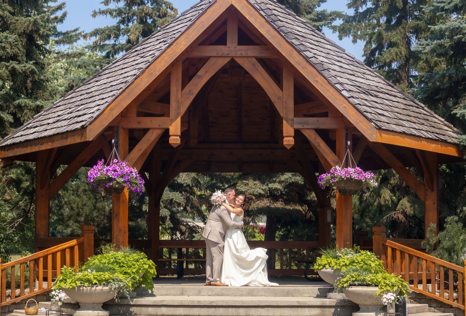 Rustic wooden pavilion with cedar shake roof and exposed beams surrounded by evergreen trees.