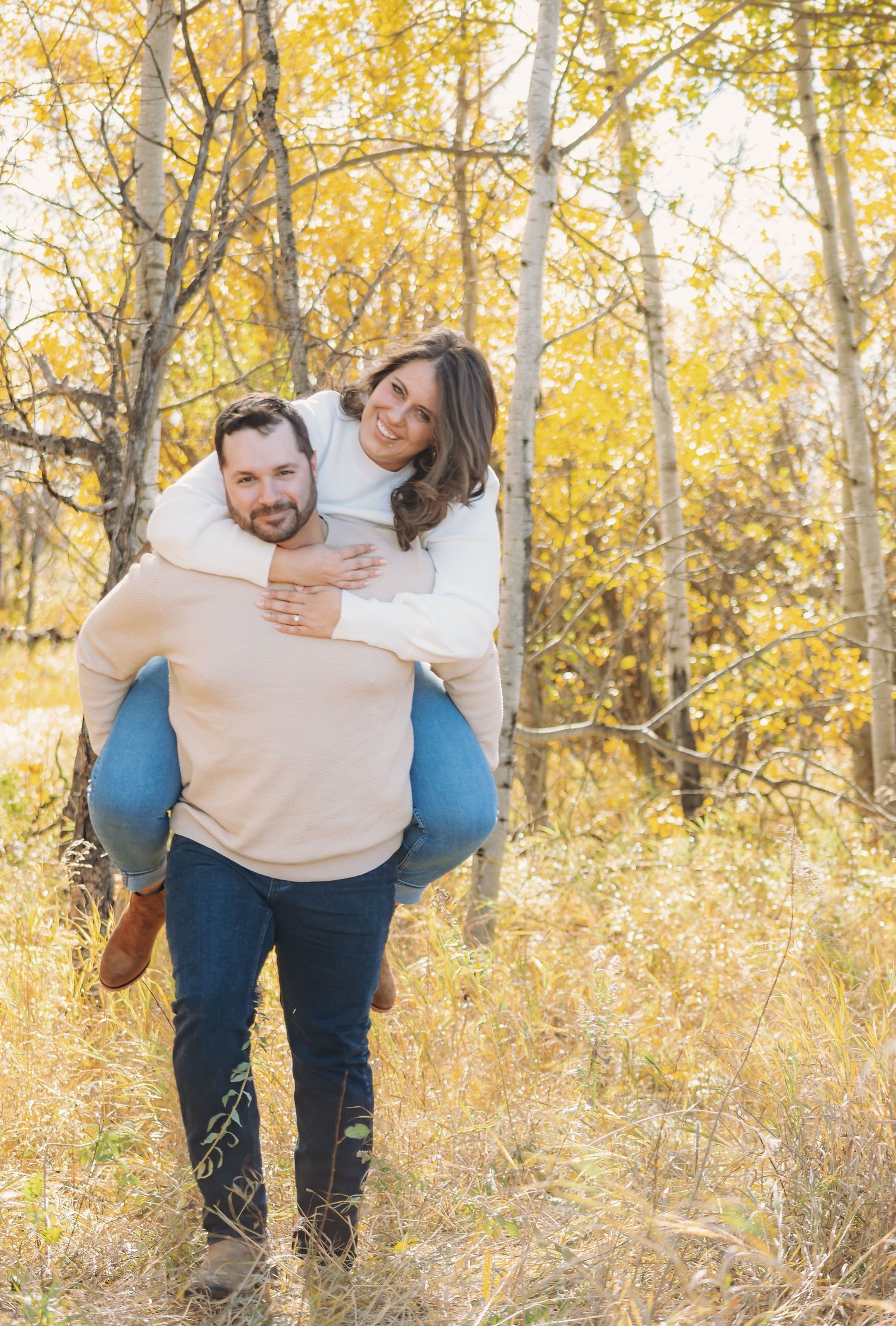 Playful couple poses in a golden aspen forest during autumn.