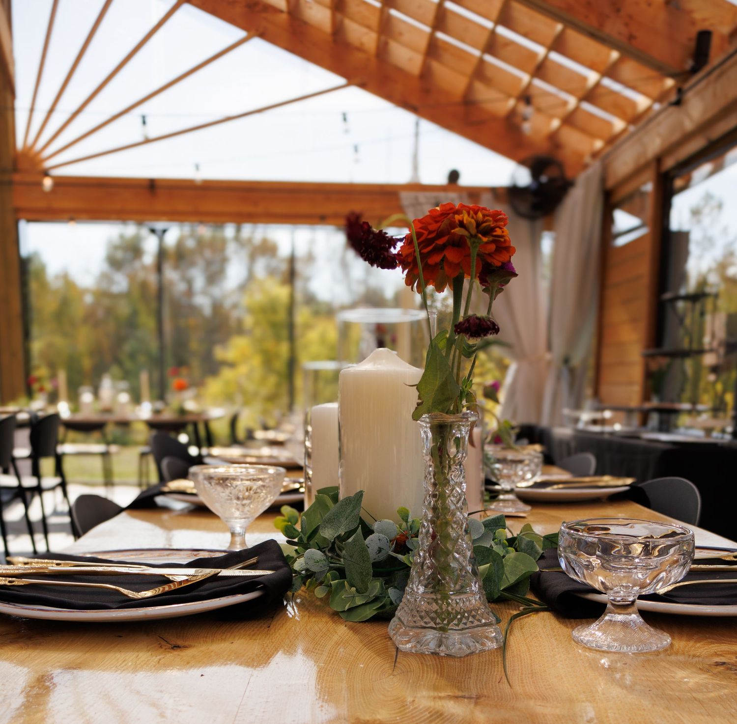 Elegant wedding reception table settings with crystal glasses and wooden beams overhead in rustic venue.