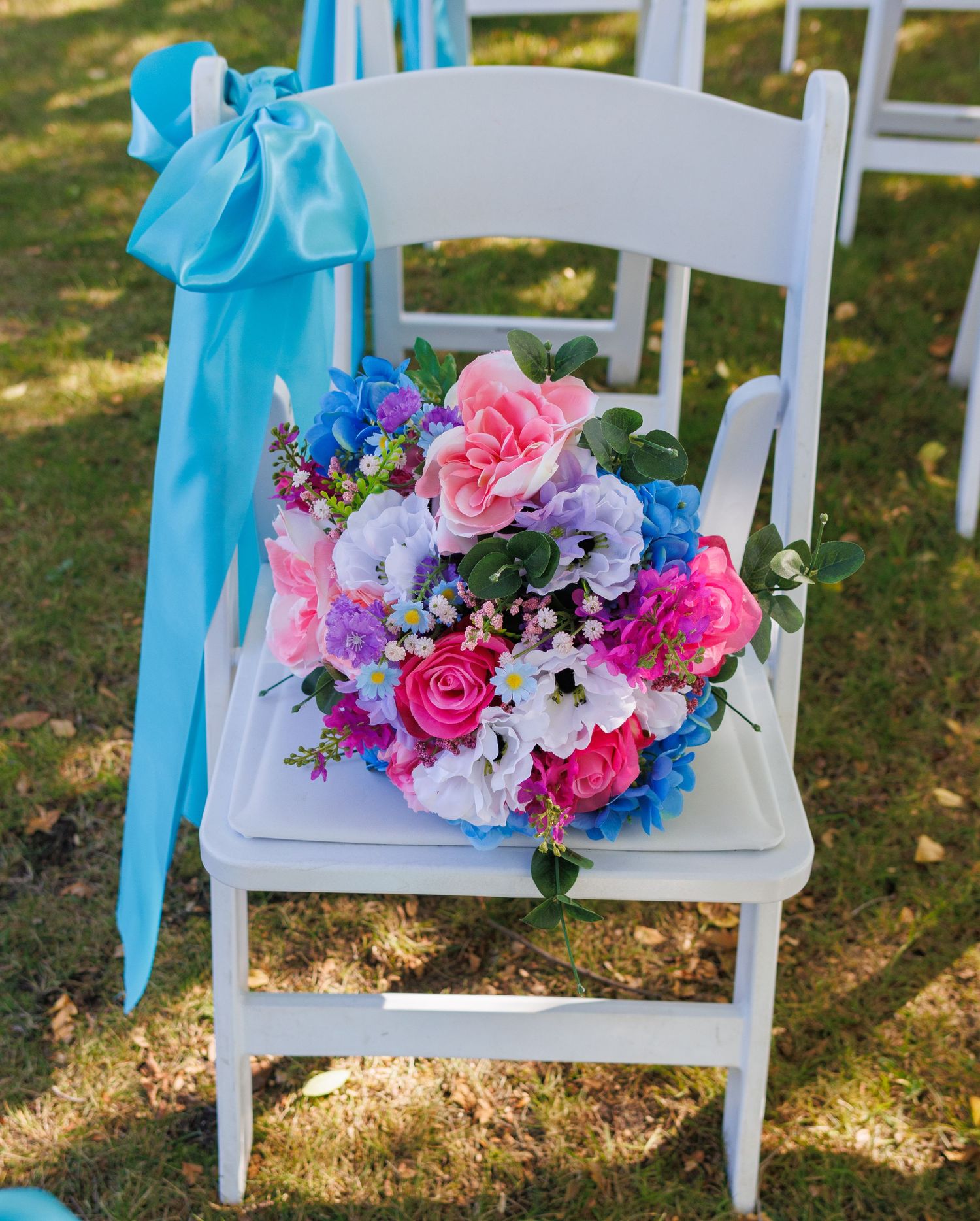 White chairs decorated with turquoise bows and colorful floral arrangements for outdoor ceremony.