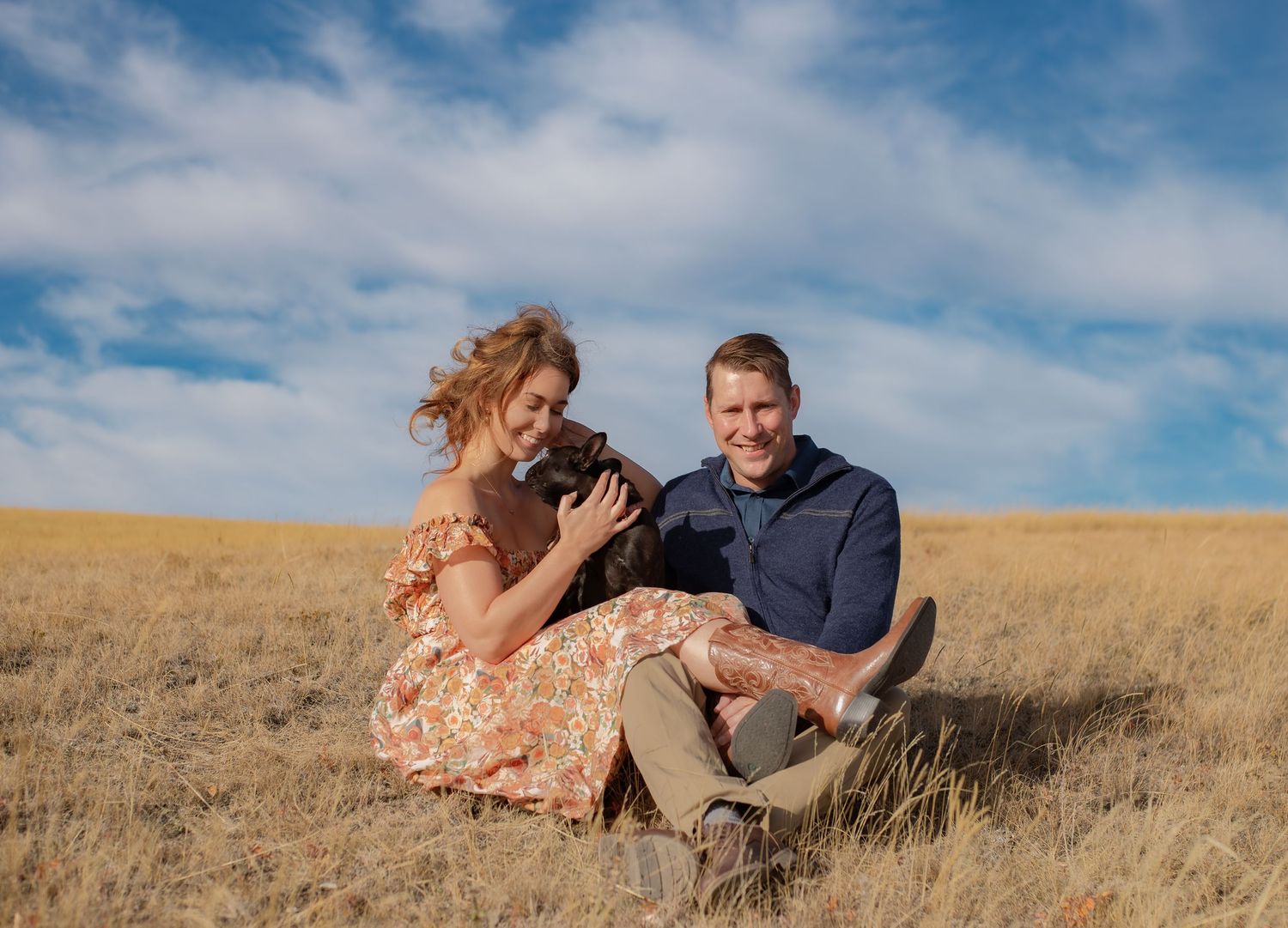 Couple sitting in golden prairie field with their dog during a sunny afternoon.