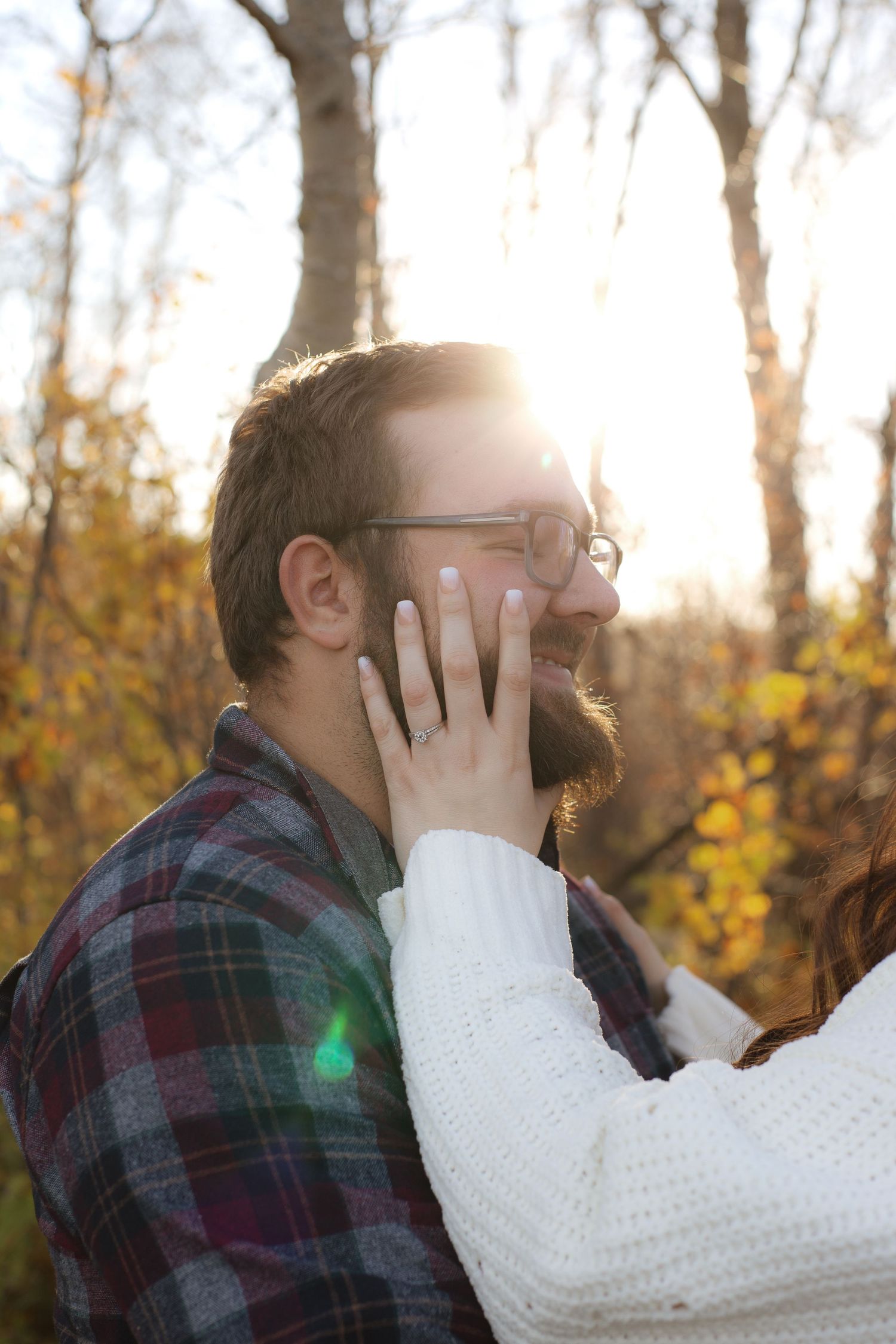 A tender moment captured in autumn sunlight as a hand gently touches a person wearing glasses and plaid.