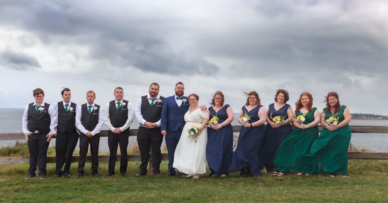 A wedding party poses together on a cloudy day by the ocean.