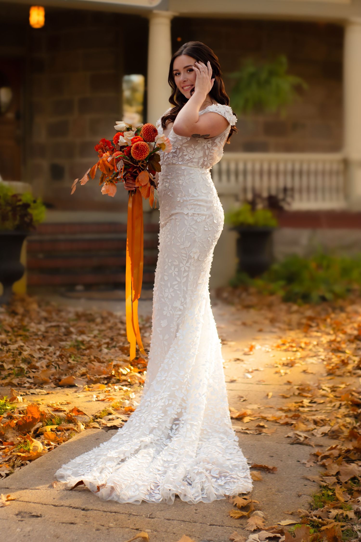 Elegant lace wedding dress with train photographed on porch with autumn leaves.
