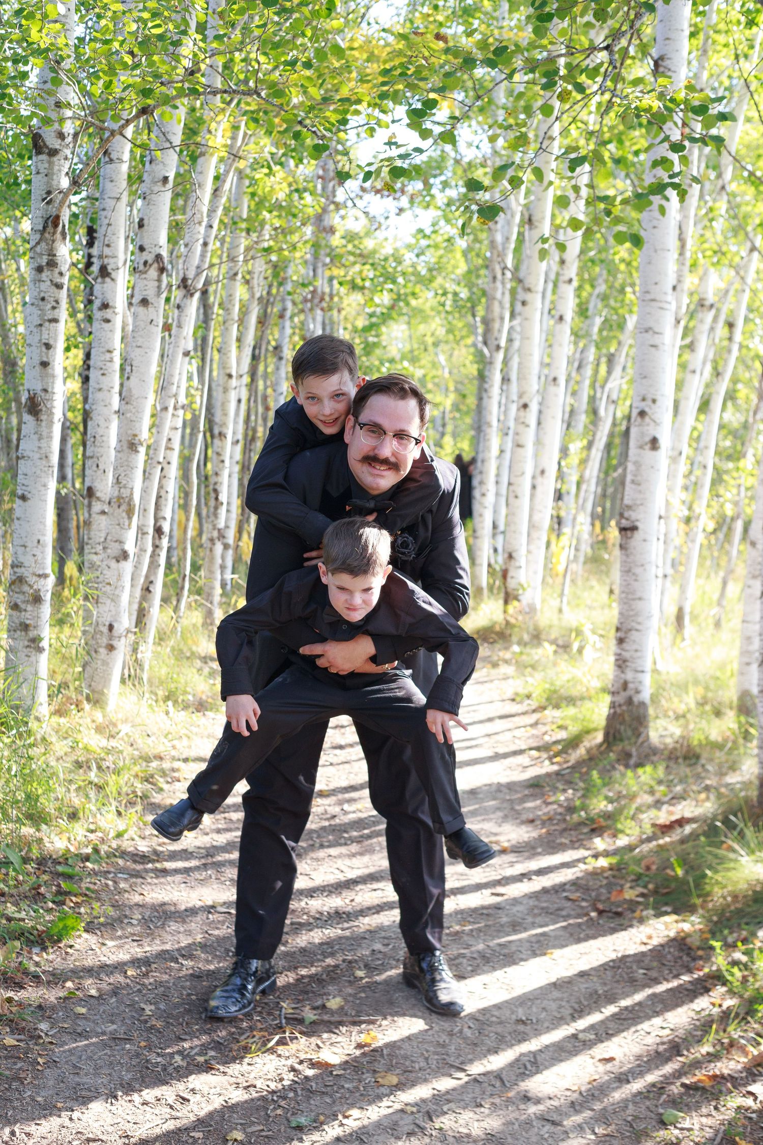 Wedding party members playfully pose in birch tree forest.