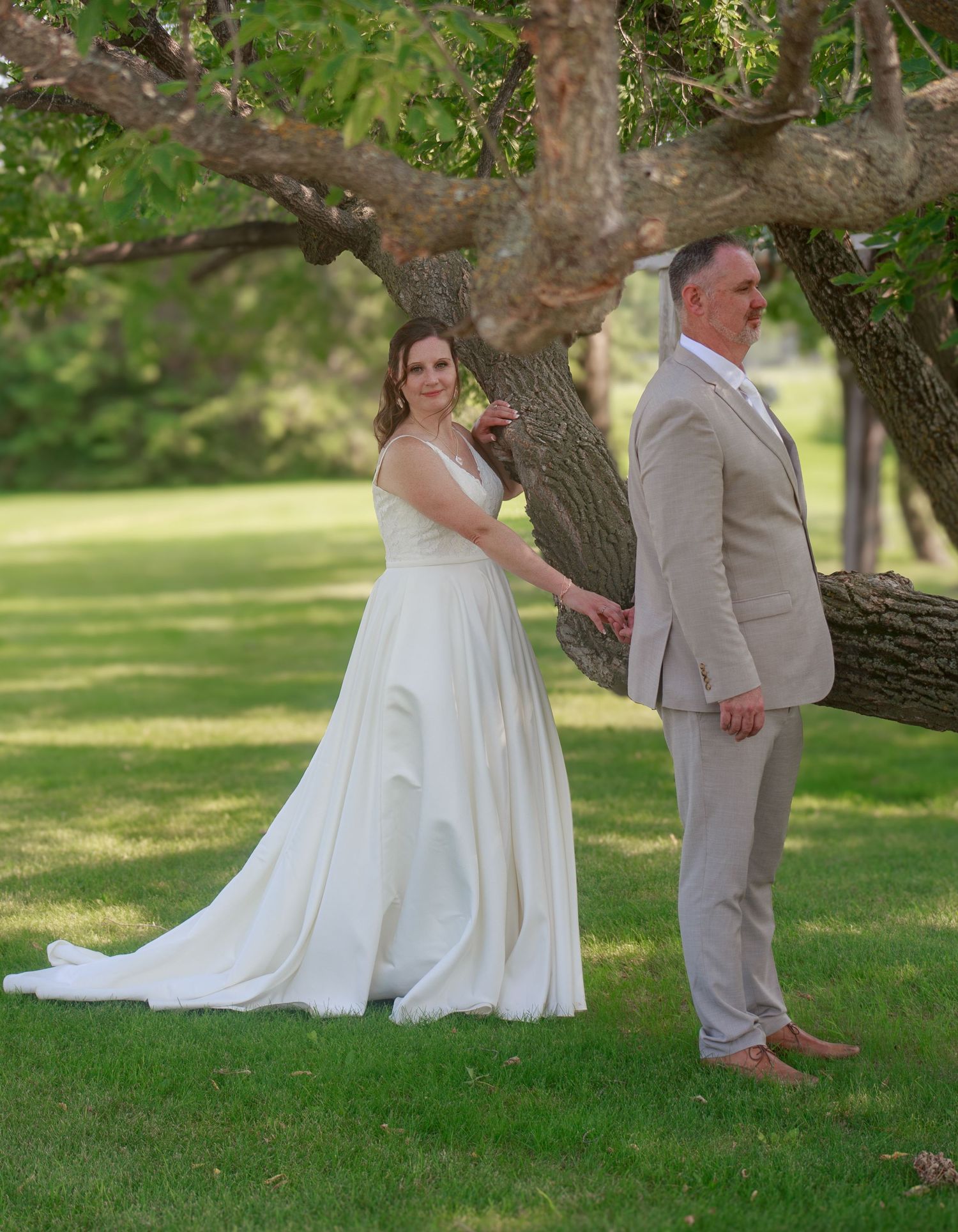 A romantic first look moment between newlyweds under a large tree in a garden setting.