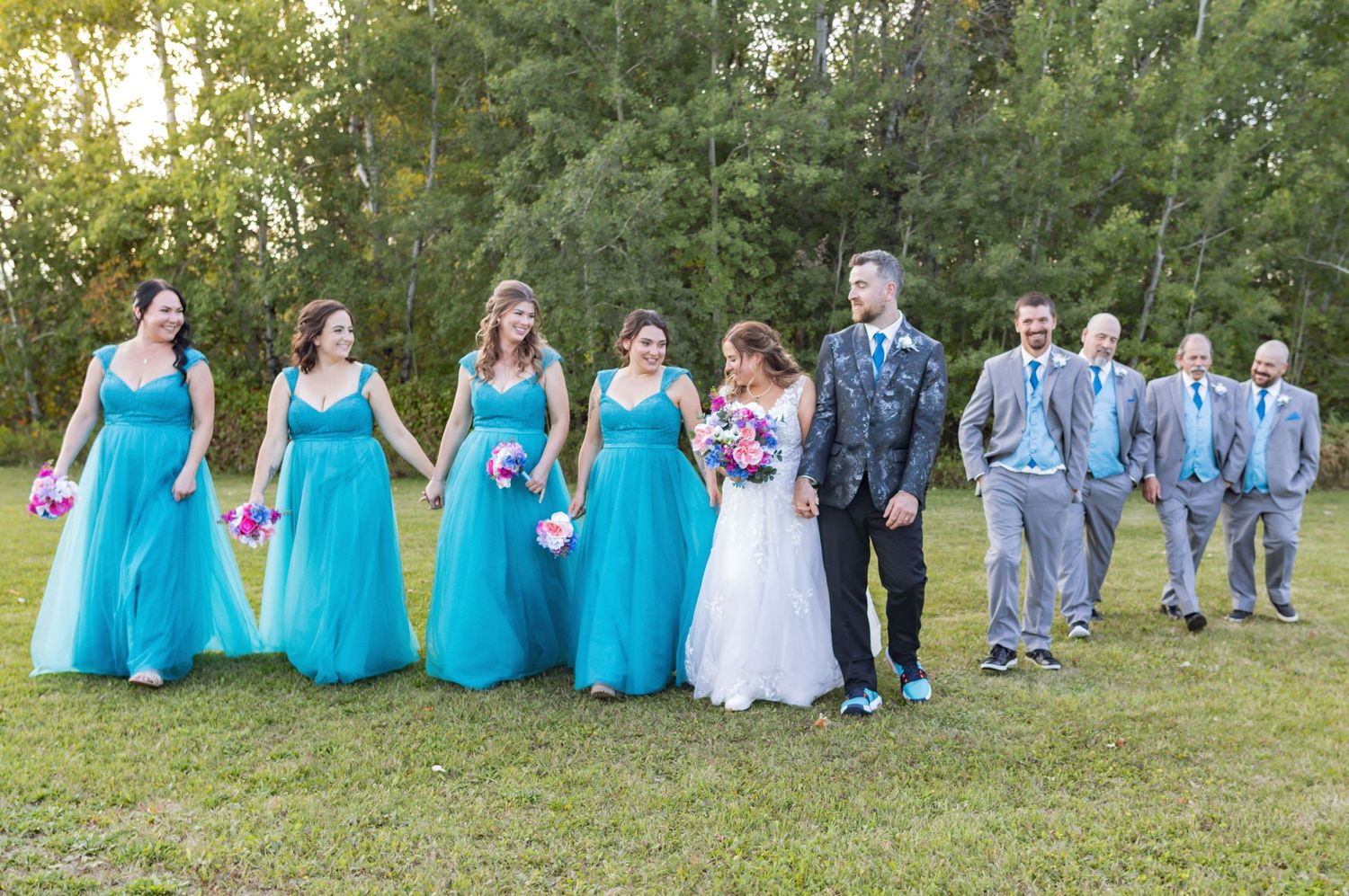 Wedding party poses in coordinated turquoise and gray attire for outdoor group photos.