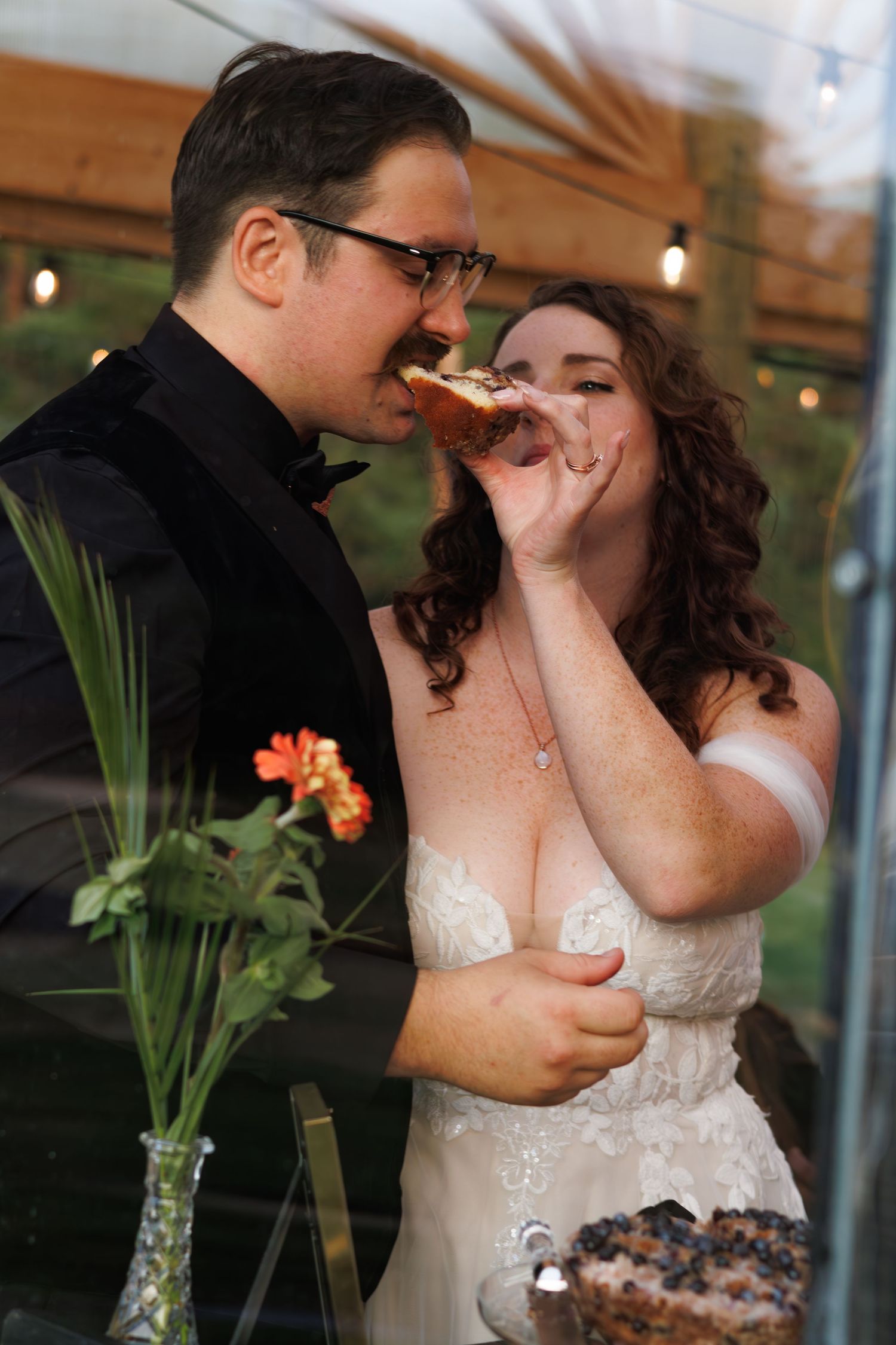 Couple shares cake during wedding reception with tropical flowers in background.