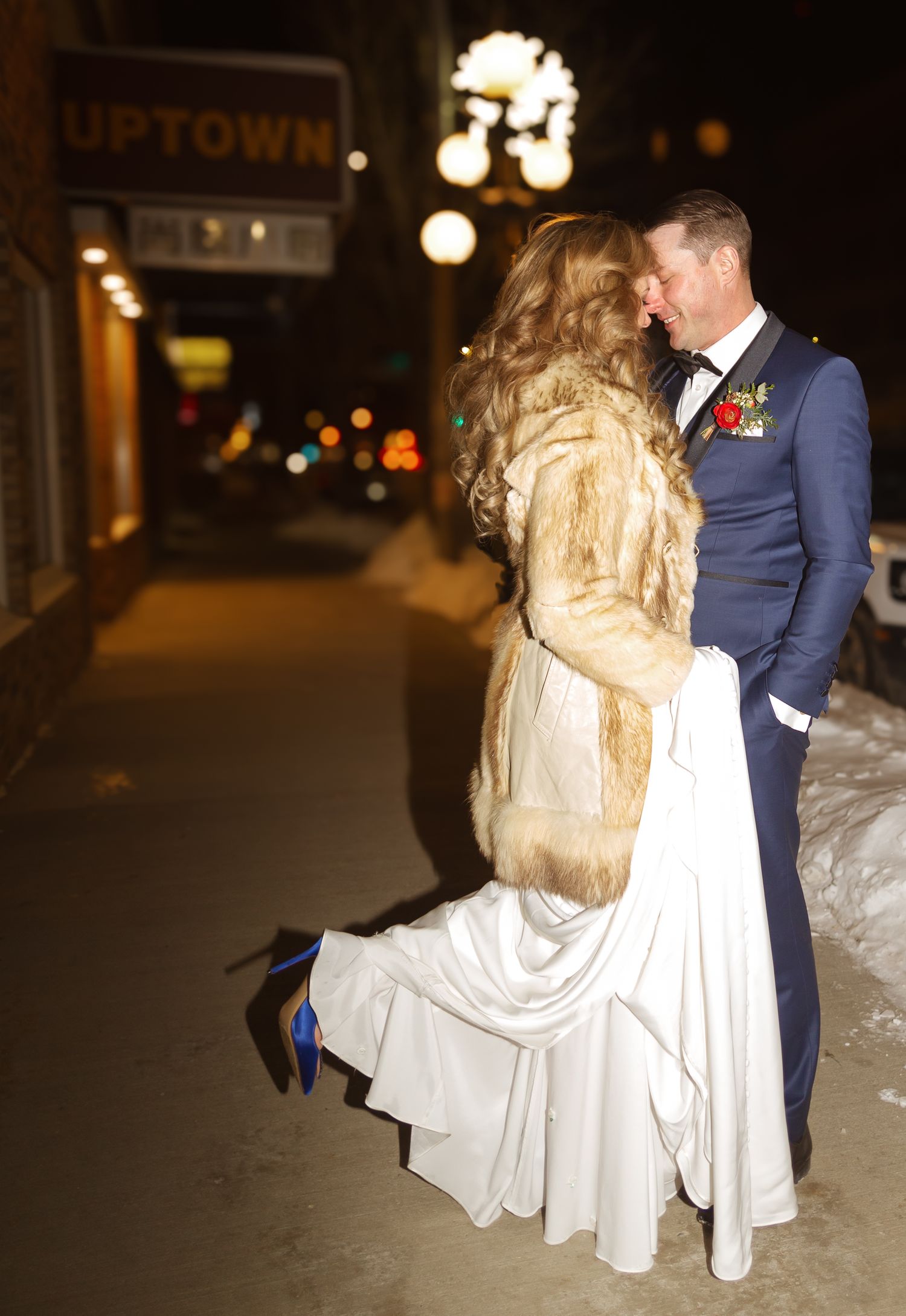 A romantic nighttime wedding portrait under illuminated street lights with a vintage fur coat.