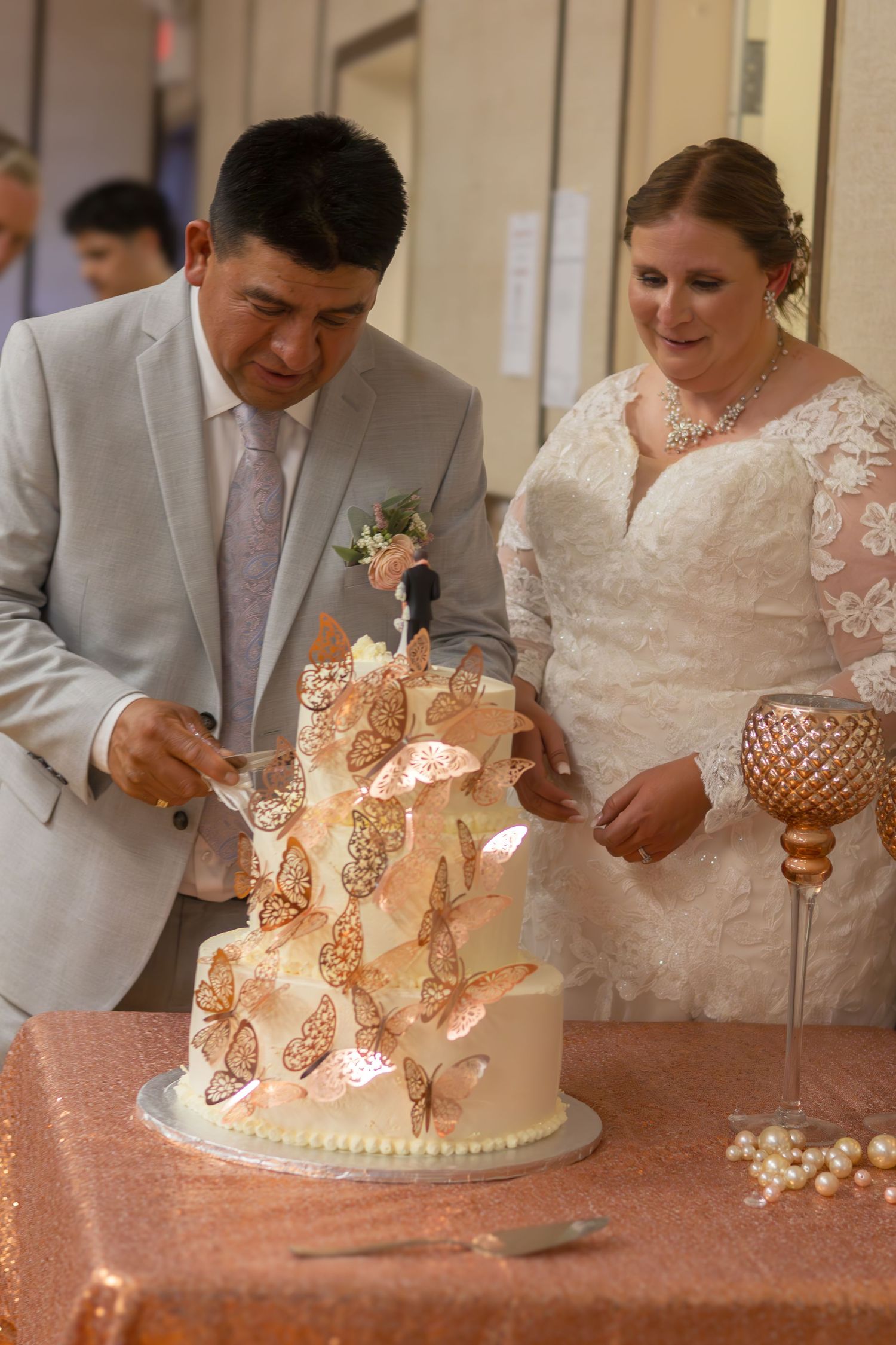 A couple cuts into their elegant butterfly-decorated wedding cake at their reception.