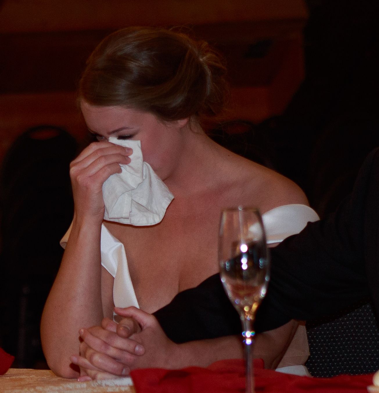 Person dabs eyes with tissue while sitting at formal dinner table.