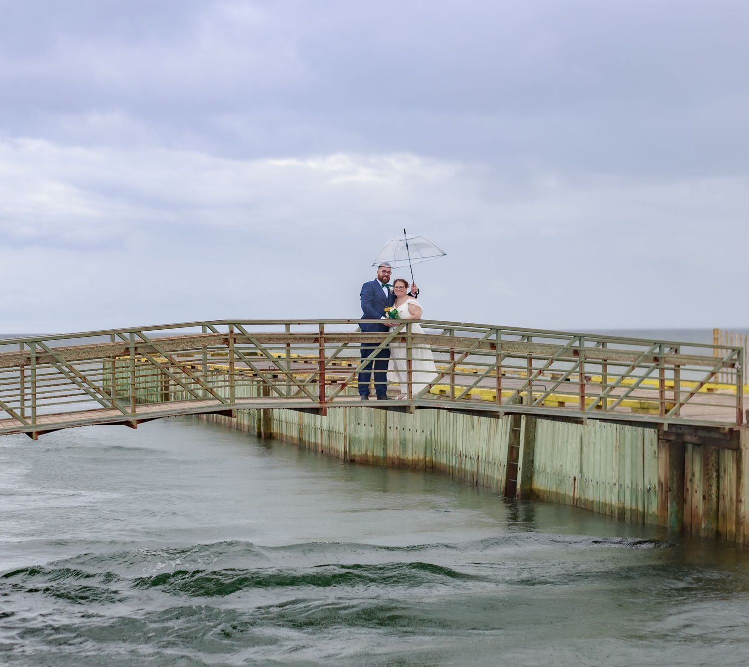 Long wooden pier extending into choppy ocean waters under overcast skies.