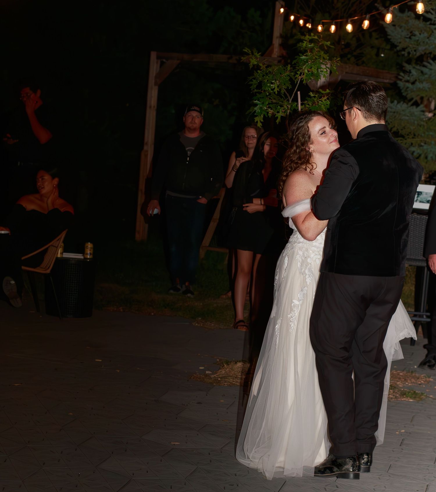 First dance under string lights at an outdoor evening wedding reception.