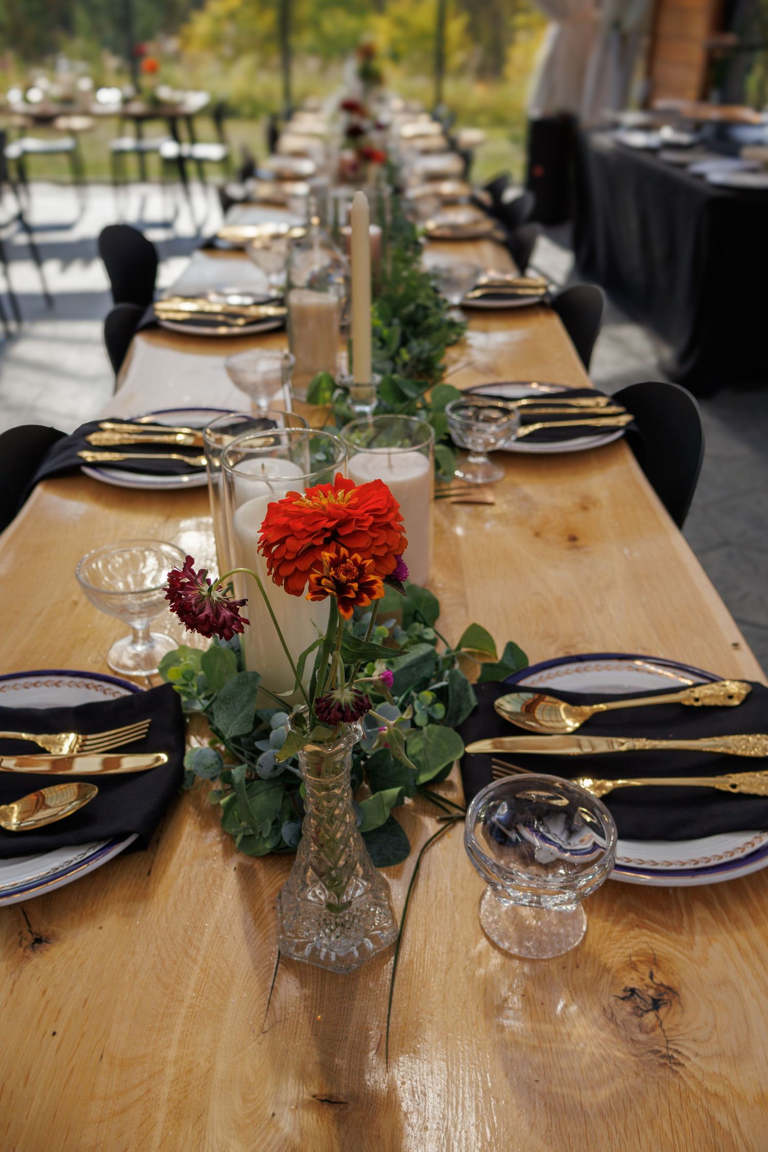 Elegant table setting with wooden tables decorated with colorful flowers, wine glasses, and black napkins.