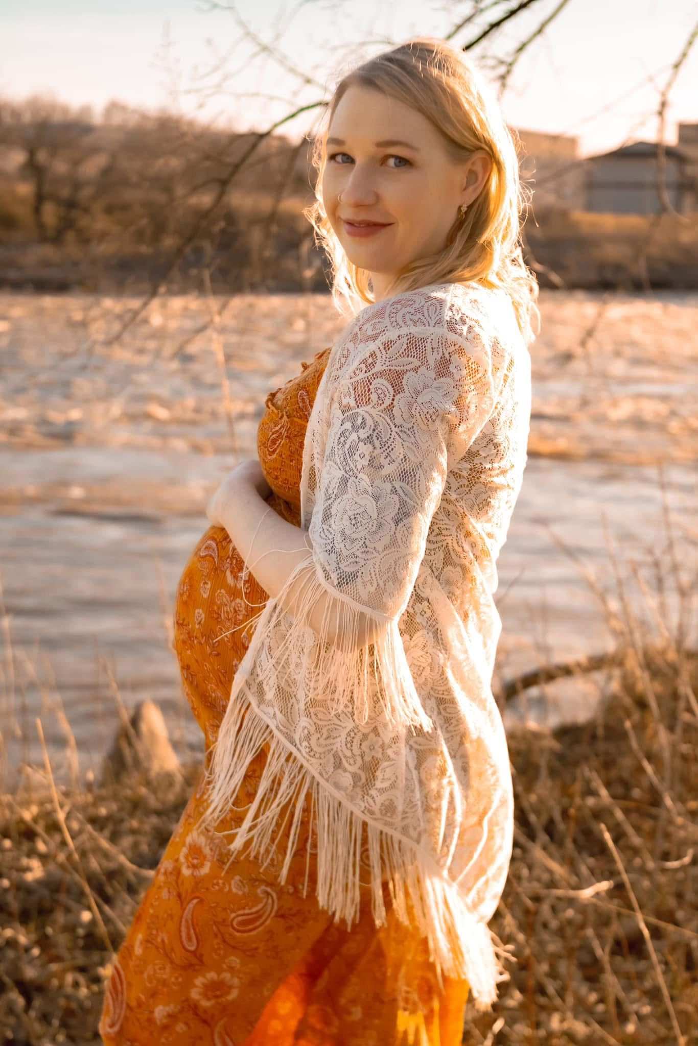 A sunset maternity photo featuring a white lace overlay and orange dress in golden light.