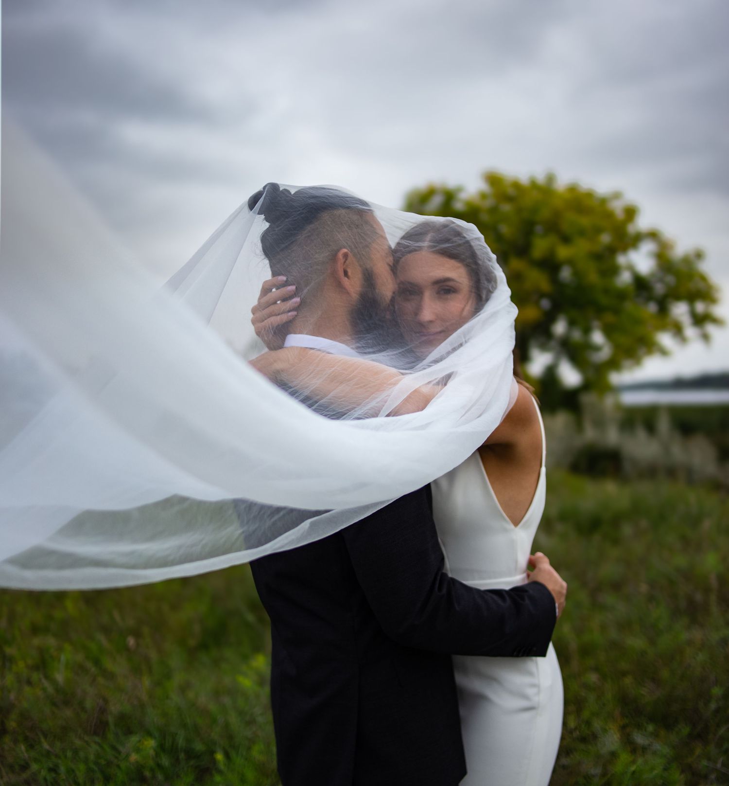 Flowing white veil creates romantic silhouette against cloudy sky in outdoor setting.