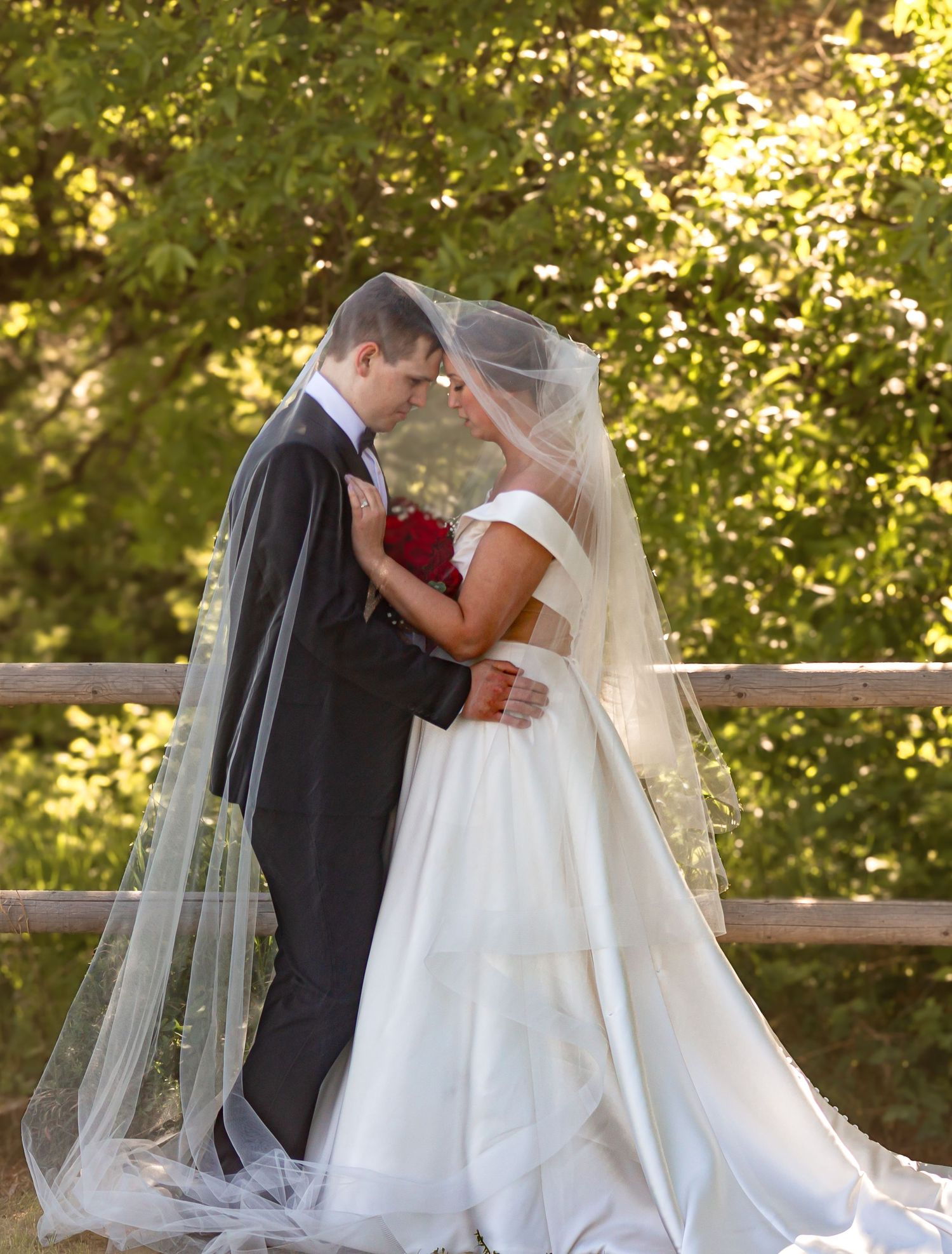 A romantic wedding couple shares a tender moment on a wooden bench.