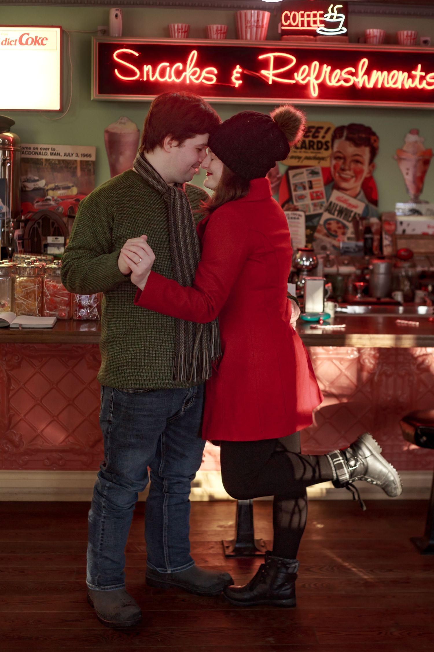 A couple shares a romantic moment in front of an illuminated snack bar counter.