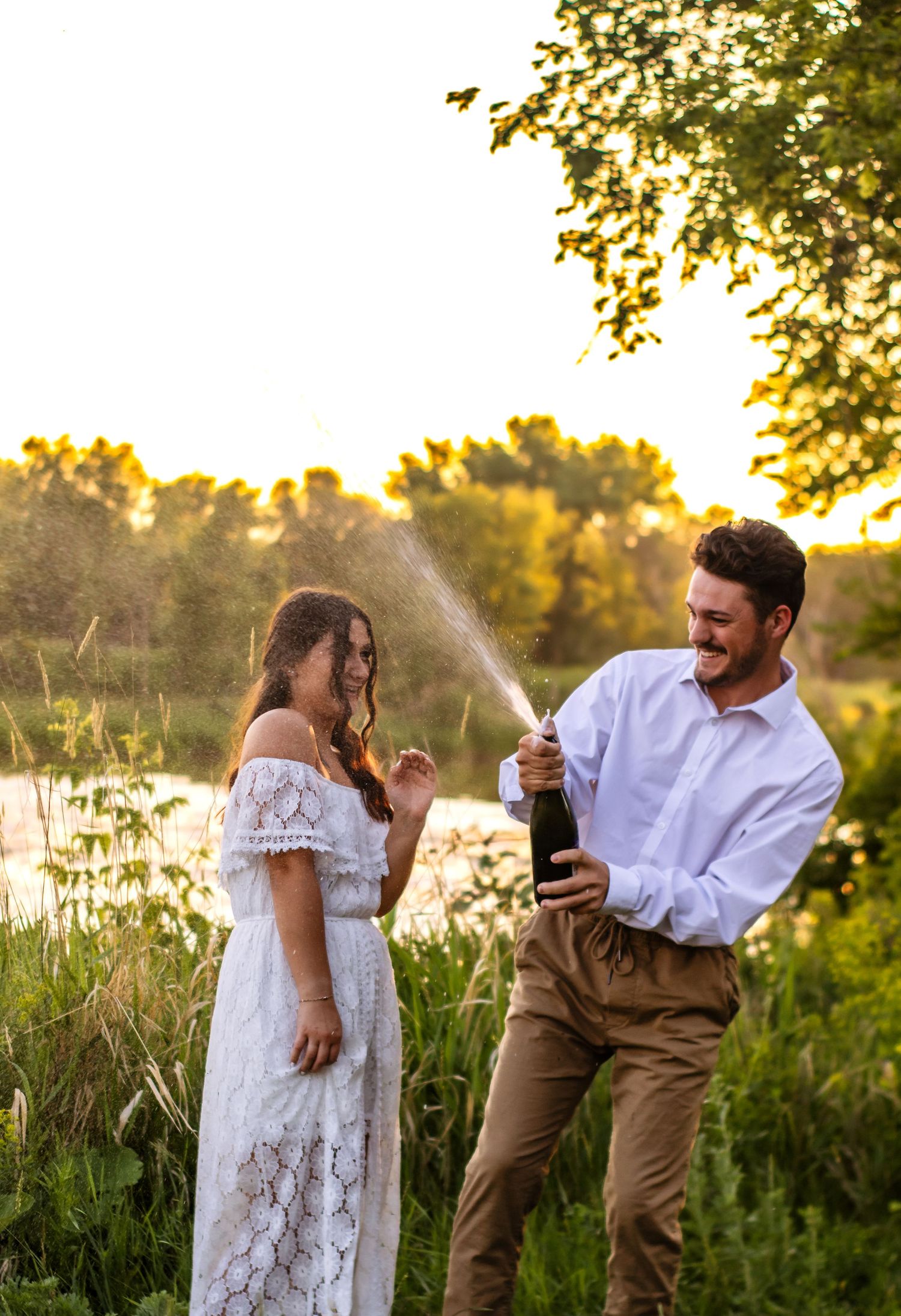 A couple celebrating with champagne in a sunny field during golden hour.
