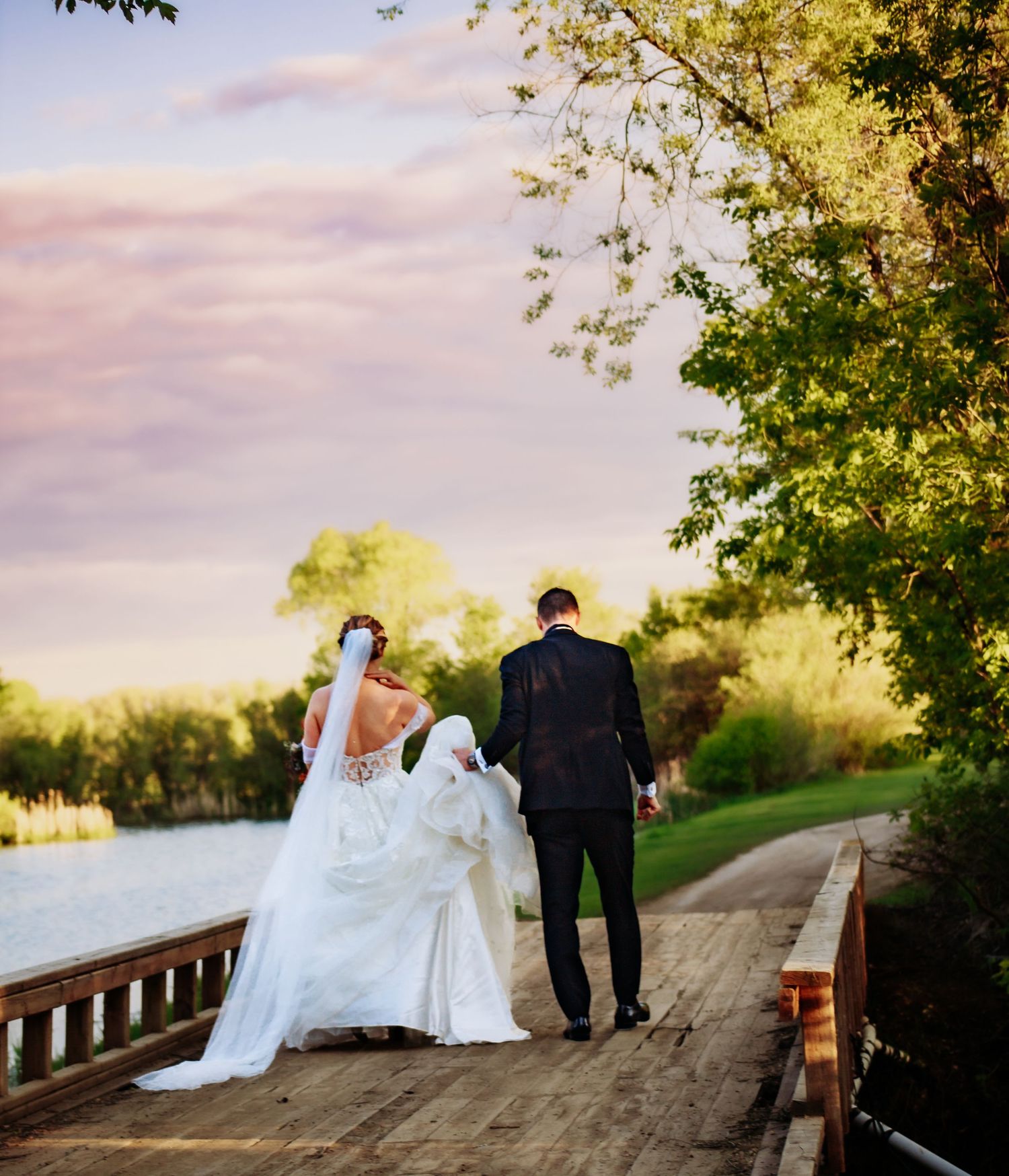 Wedding couple walking along tree-lined path during sunset.
