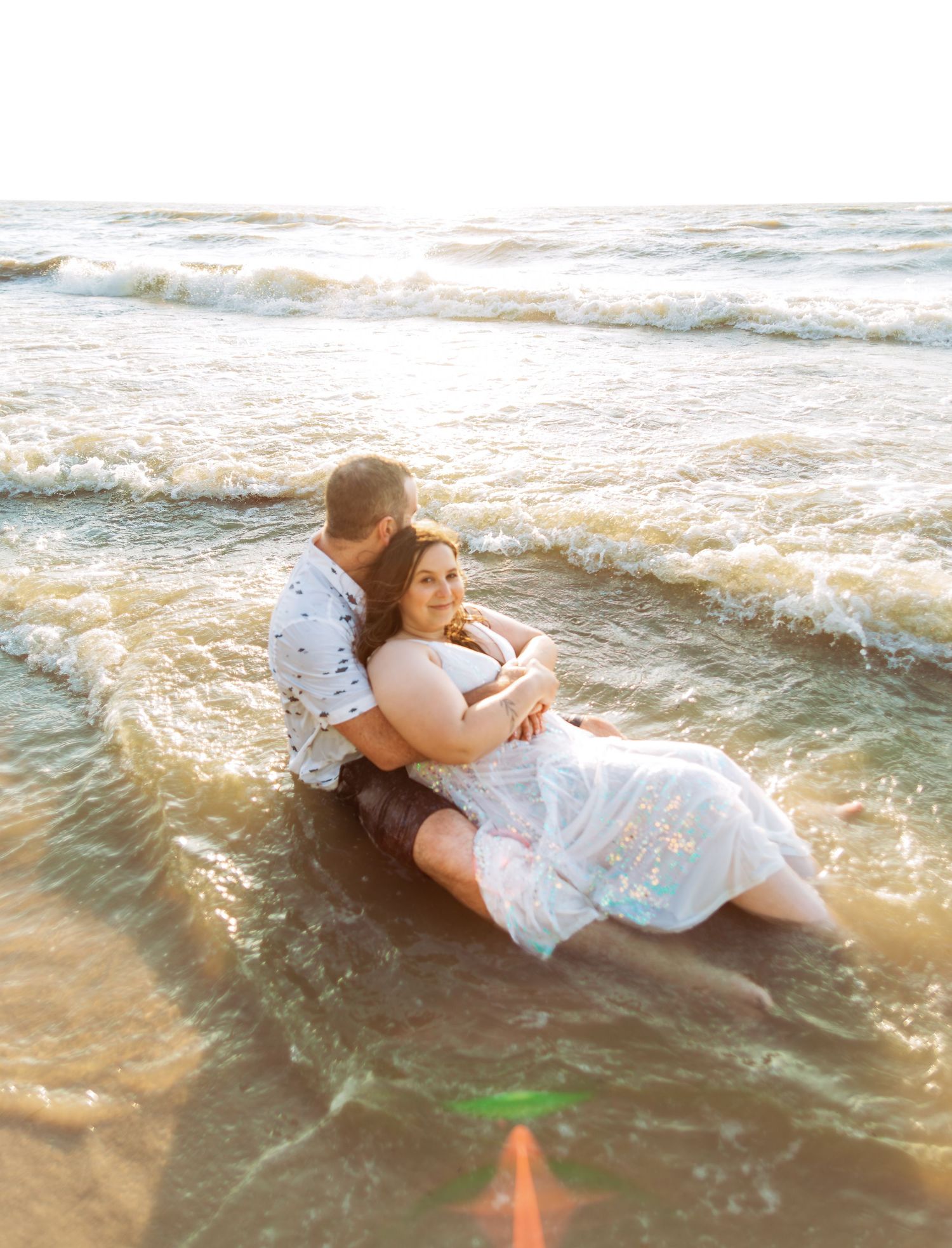 A couple relaxes in gentle ocean waves during a beach photoshoot.