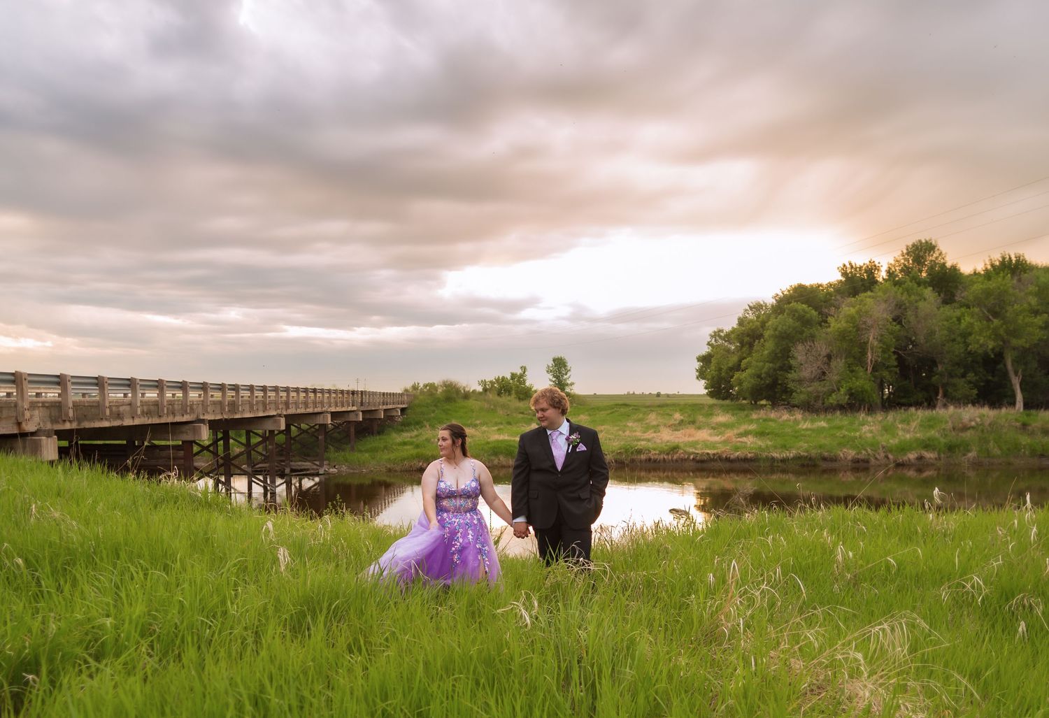 Scenic landscape with wooden bridge and grassy field under dramatic cloudy sky.