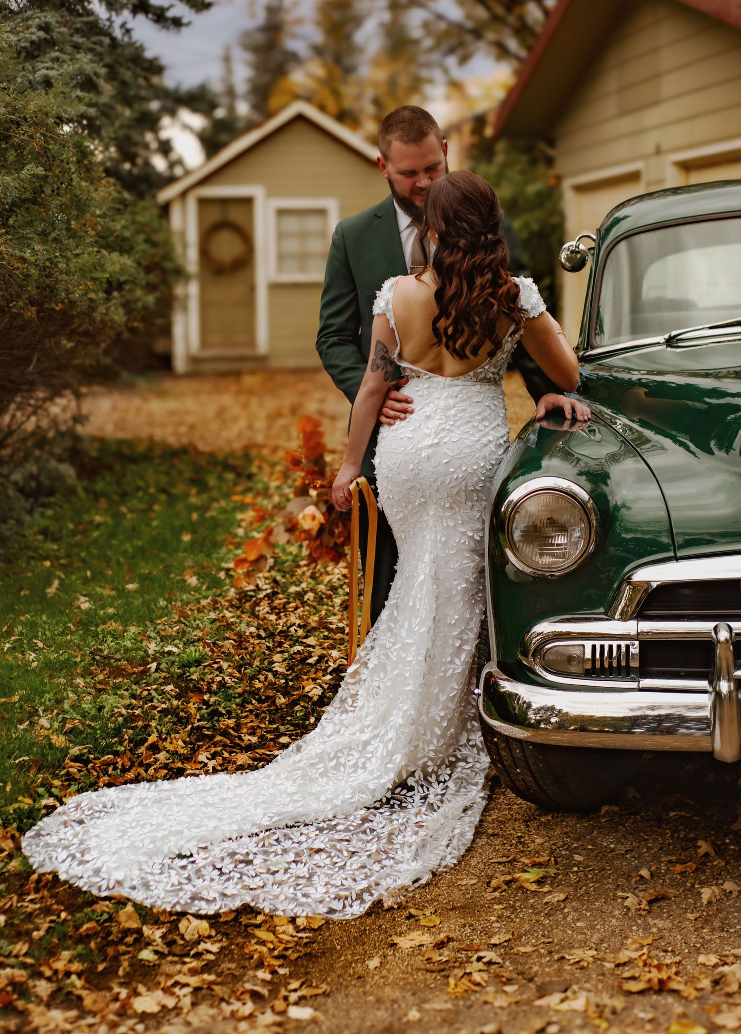 Vintage car and flowing white wedding dress detail shot with autumn leaves.