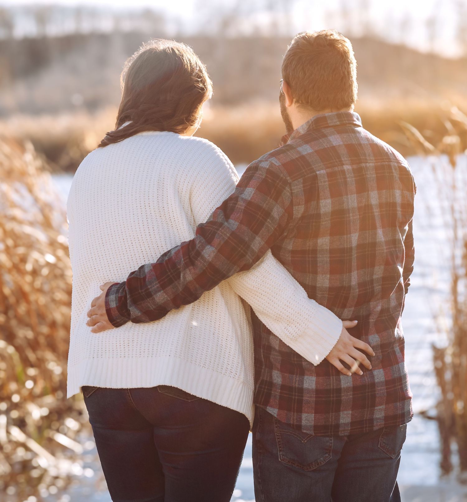 Couple in warm sweaters embrace while walking together during golden hour.