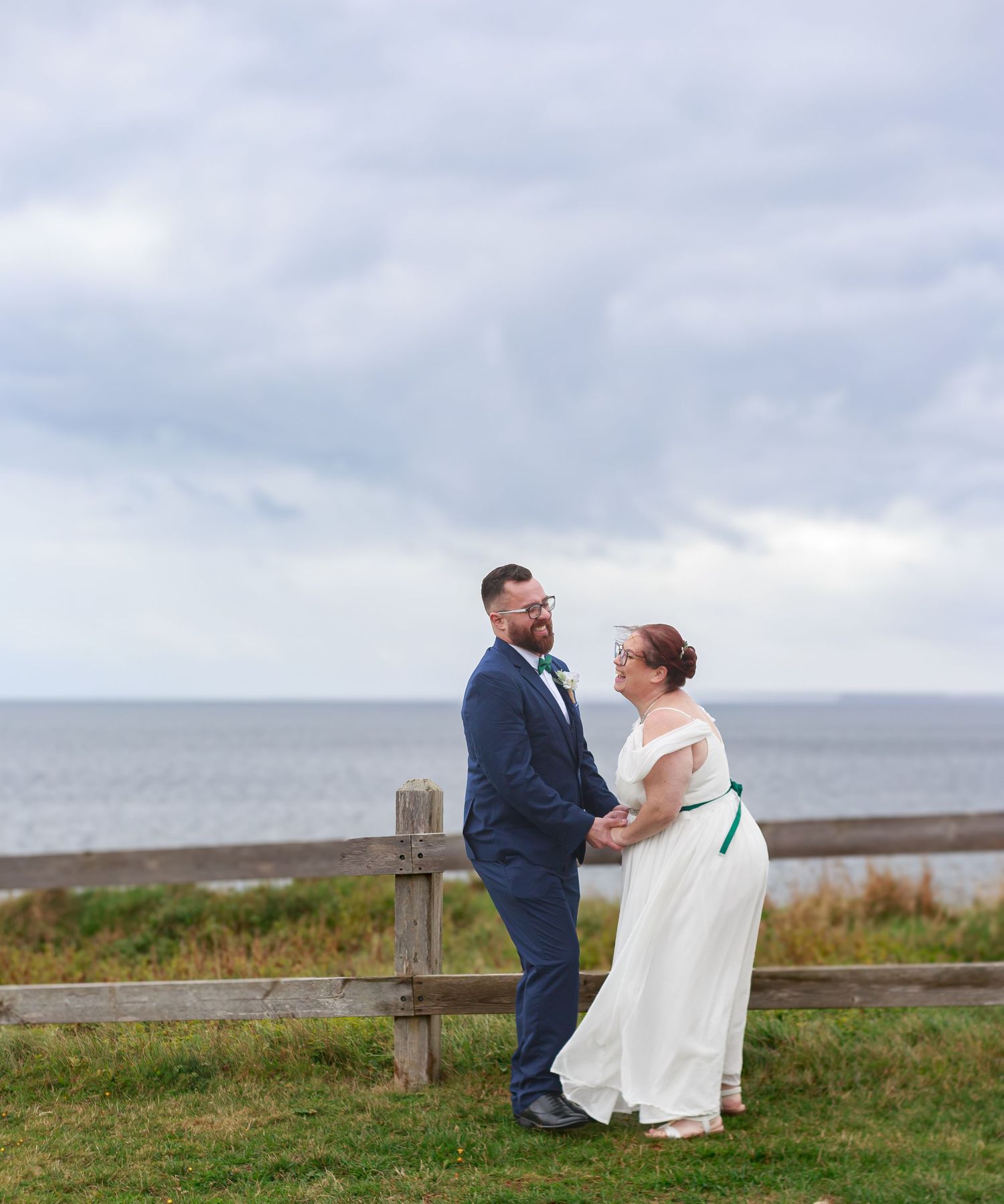 A couple shares a playful moment on a grassy cliff overlooking the ocean.