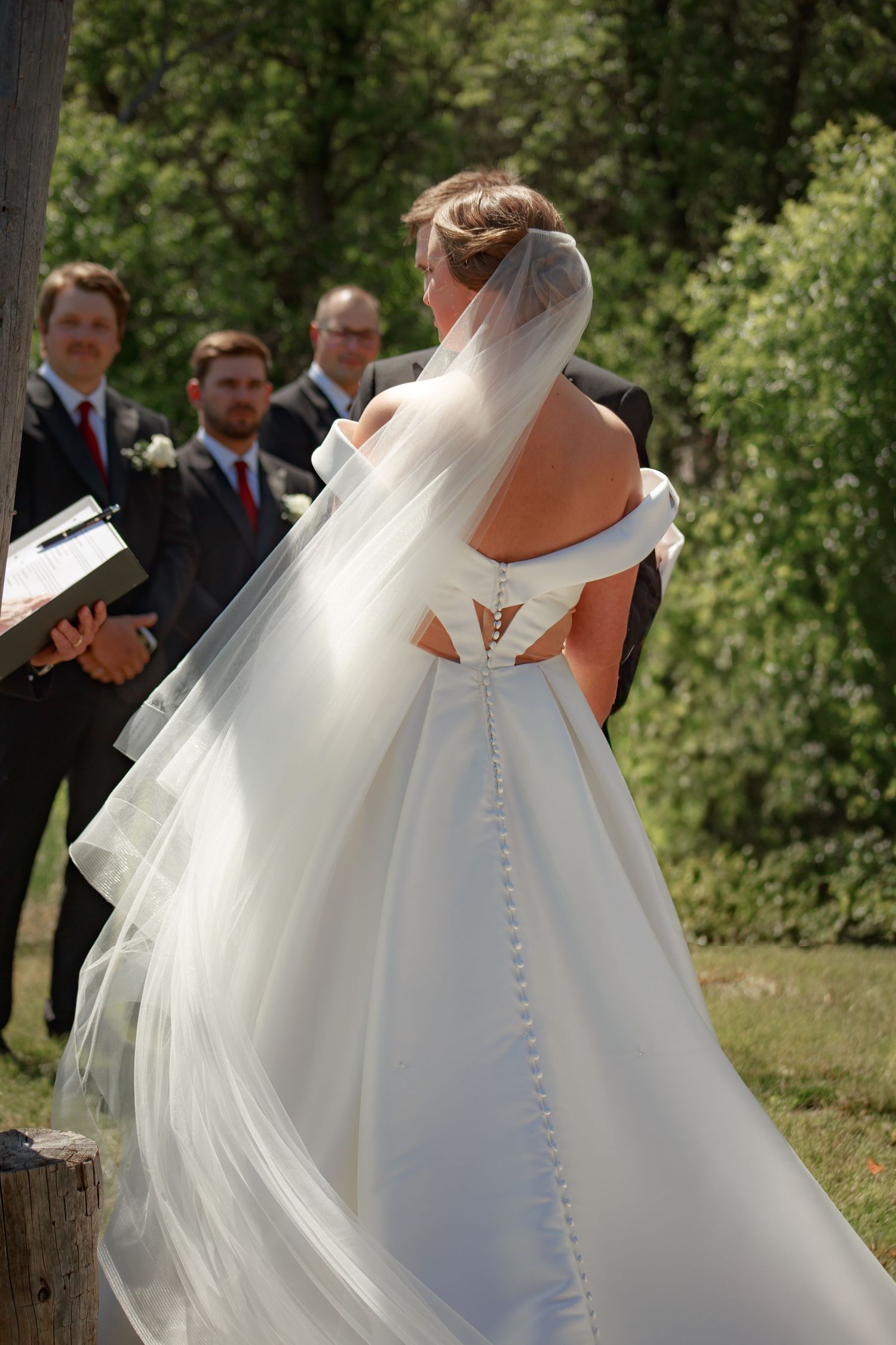 Elegant white wedding dress with button details flows gracefully in an outdoor garden setting.