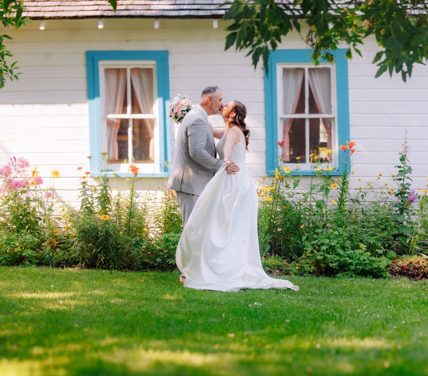 White farmhouse with blue trim windows and flowering garden in summer.