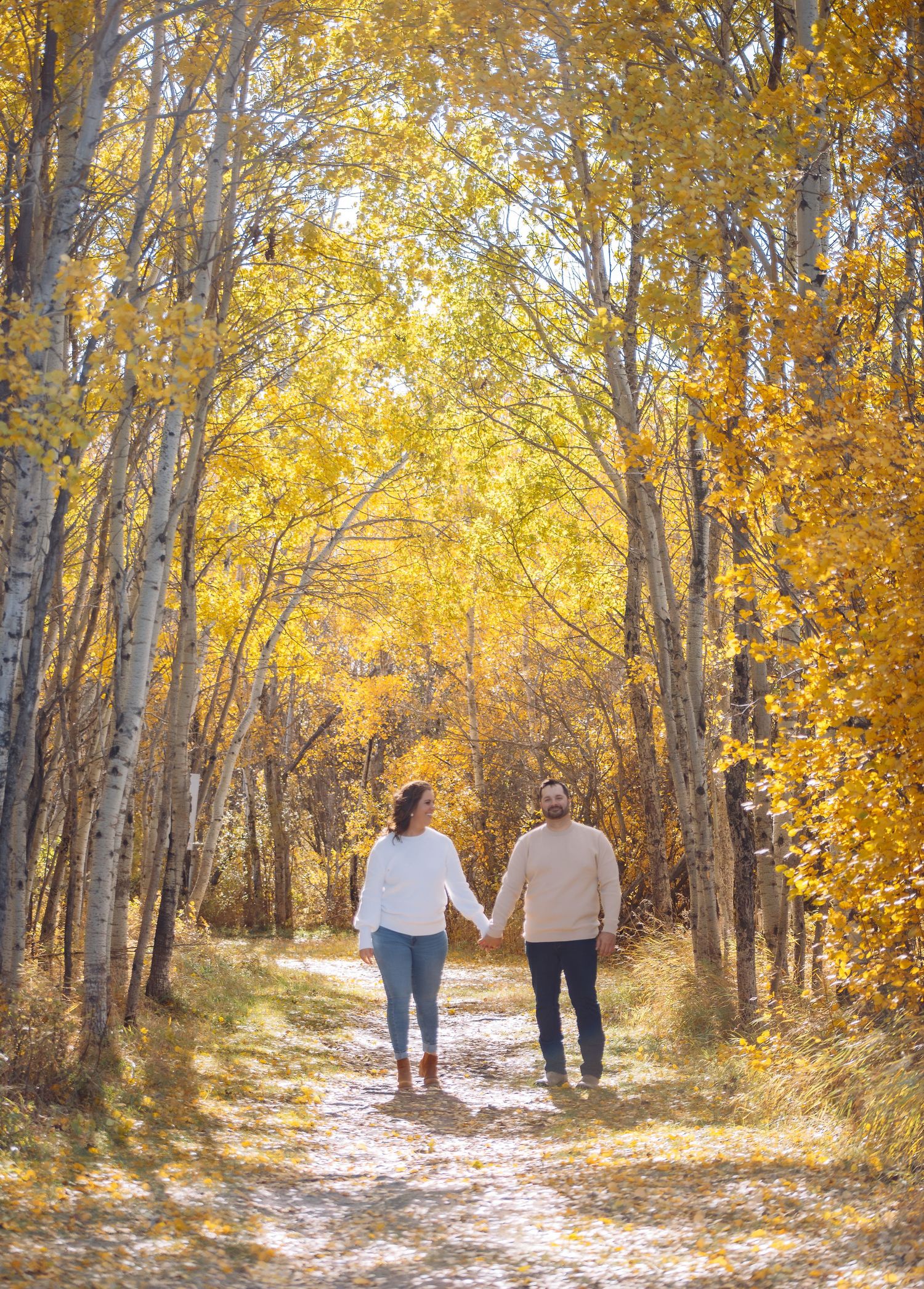 Couple strolls hand in hand down a forest trail surrounded by golden fall foliage.