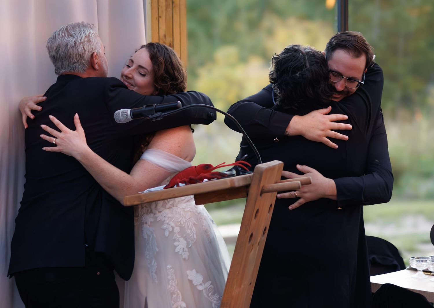 Wedding couple embraces during ceremony with guests seated on wooden benches.