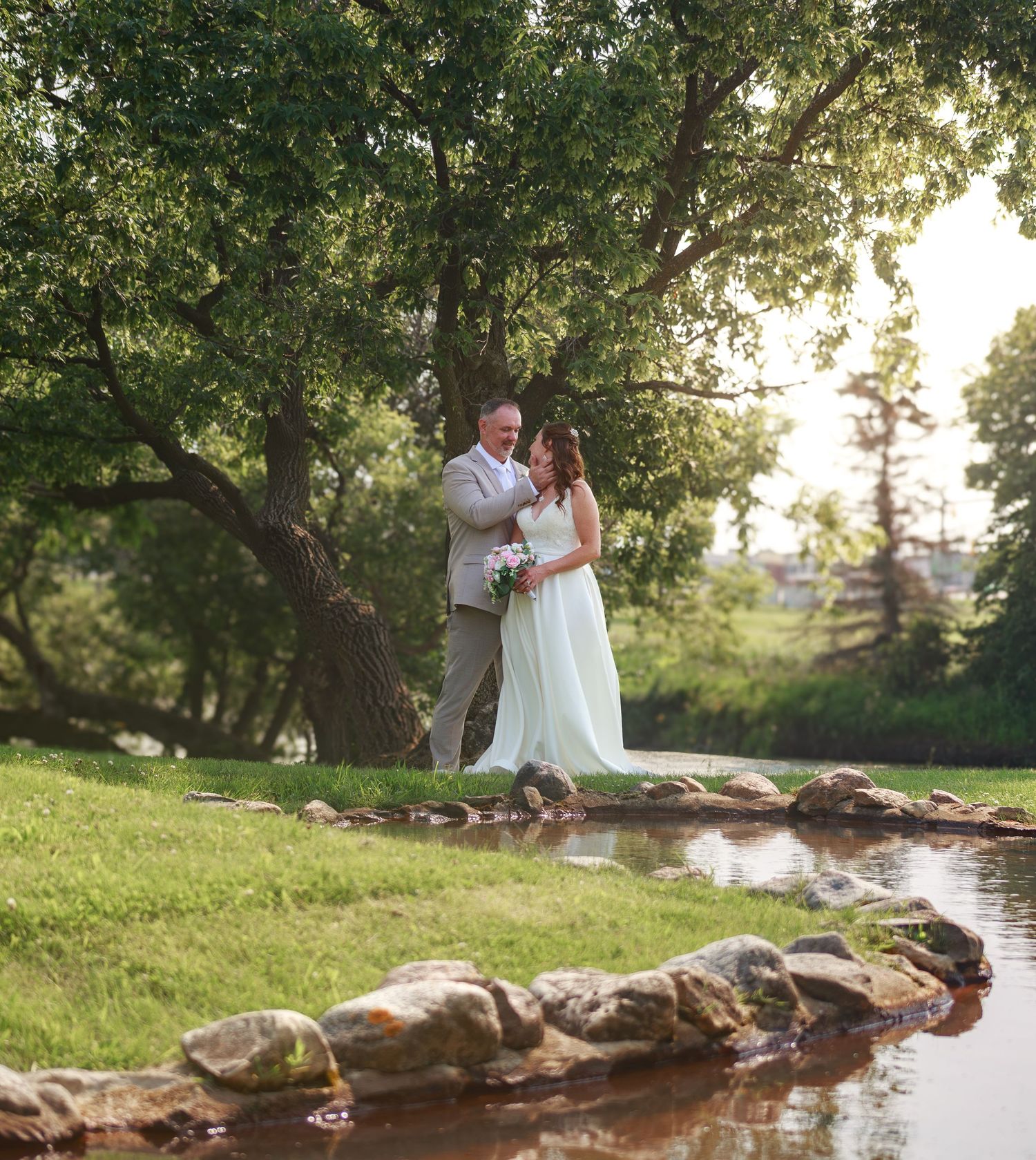 A wedding photoshoot in a scenic park setting with a winding creek and lush trees.